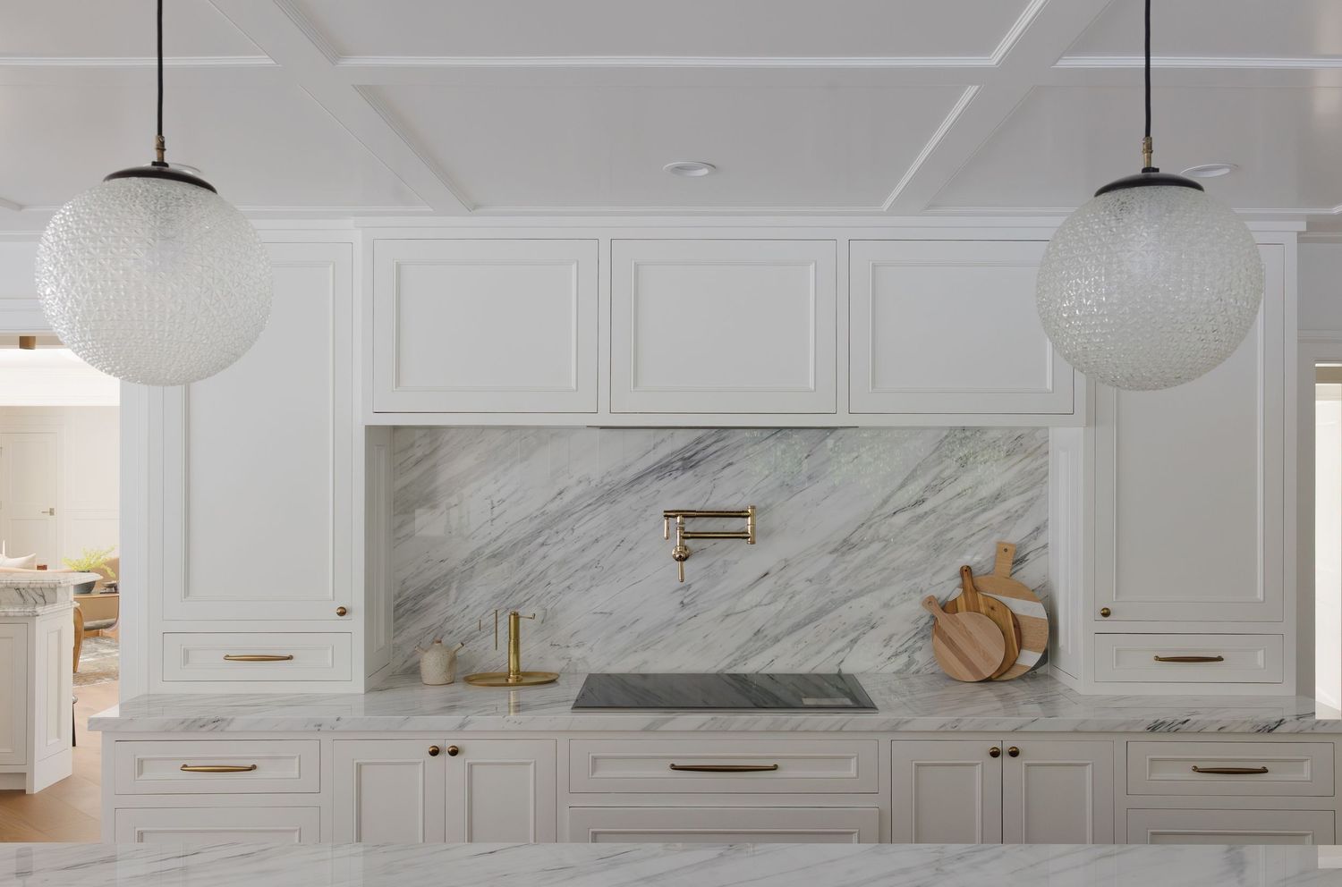 Elegant white kitchen with marble backsplash, brass pot filler, globe pendant lights, and shaker cabinets.