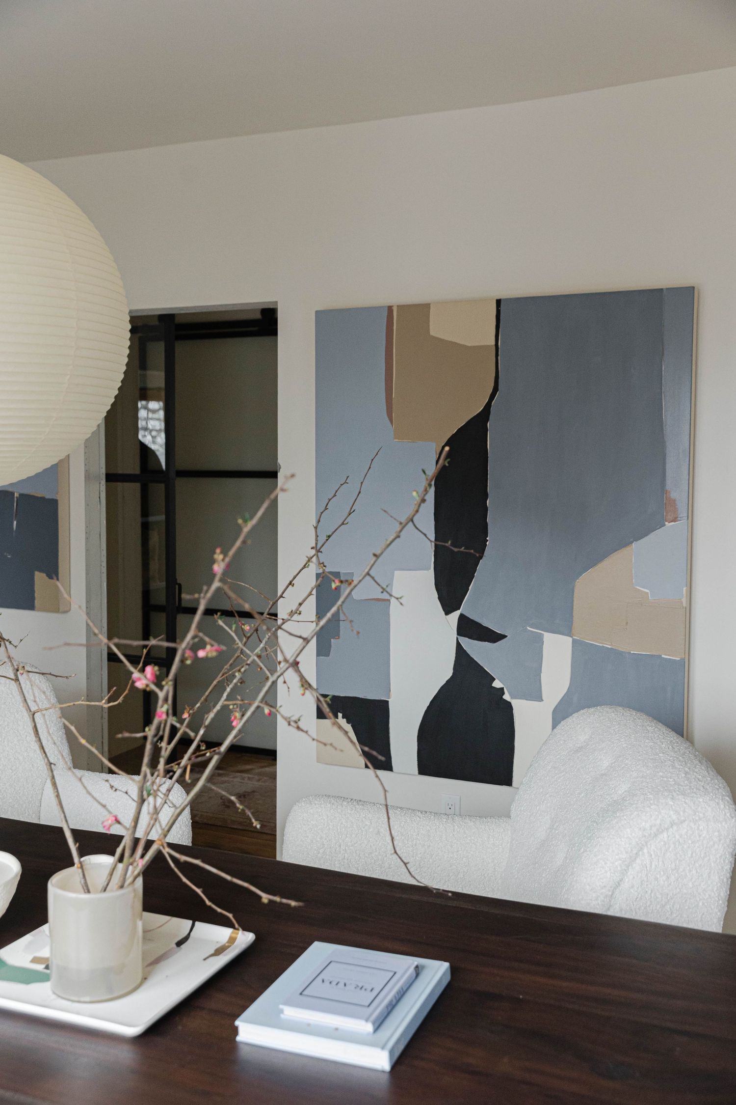 Modern living room with abstract wall art, white boucle sofa, cherry blossom branches in vase, and coffee table books.