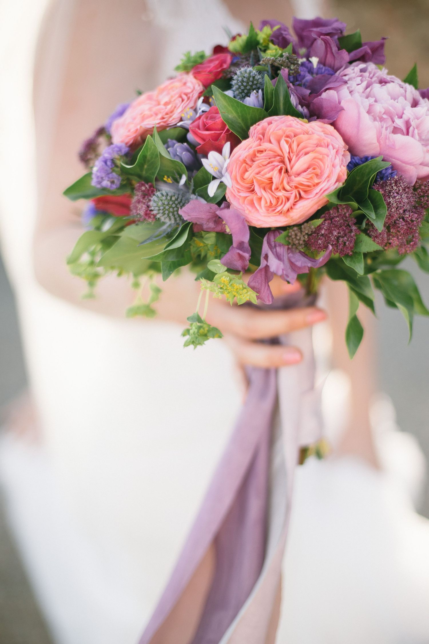 Stunning bridal bouquet with coral roses and purple flowers tied with lavender ribbon.