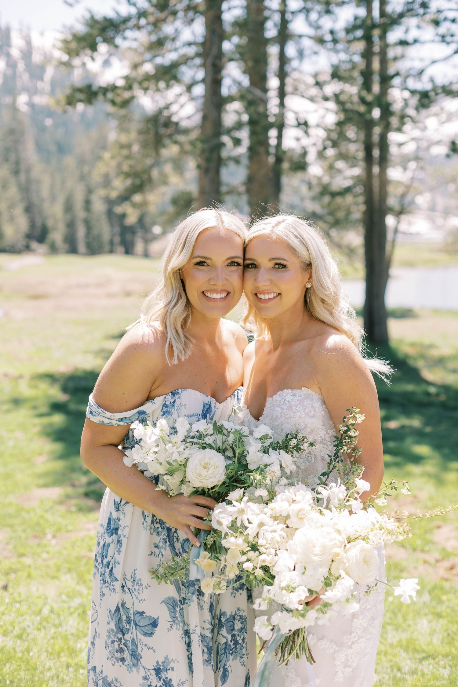 Two women in wedding attire share a joyful moment while holding white floral bouquets.