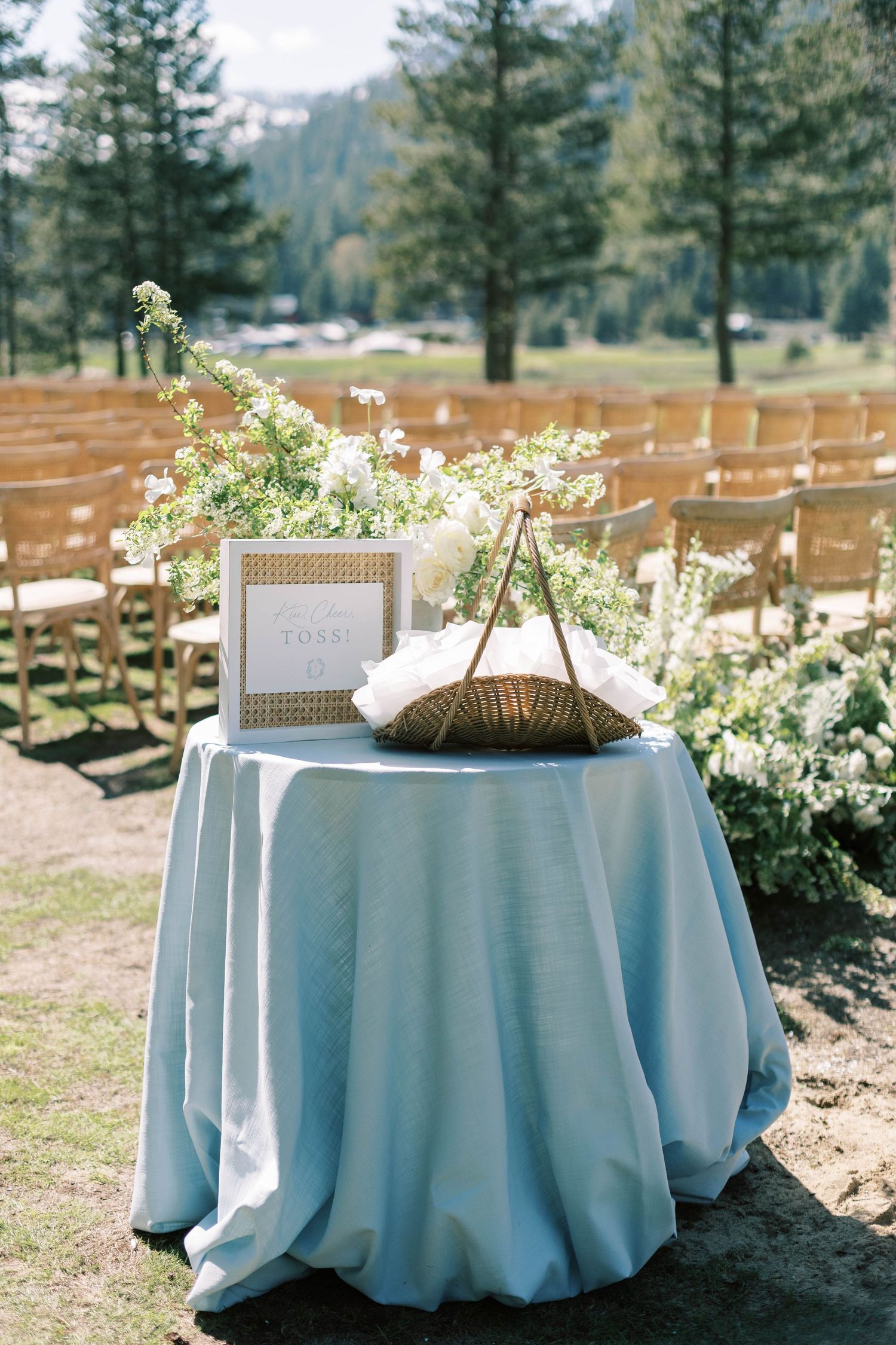 Wedding ceremony details with blue tablecloth and floral decorations against mountain backdrop.