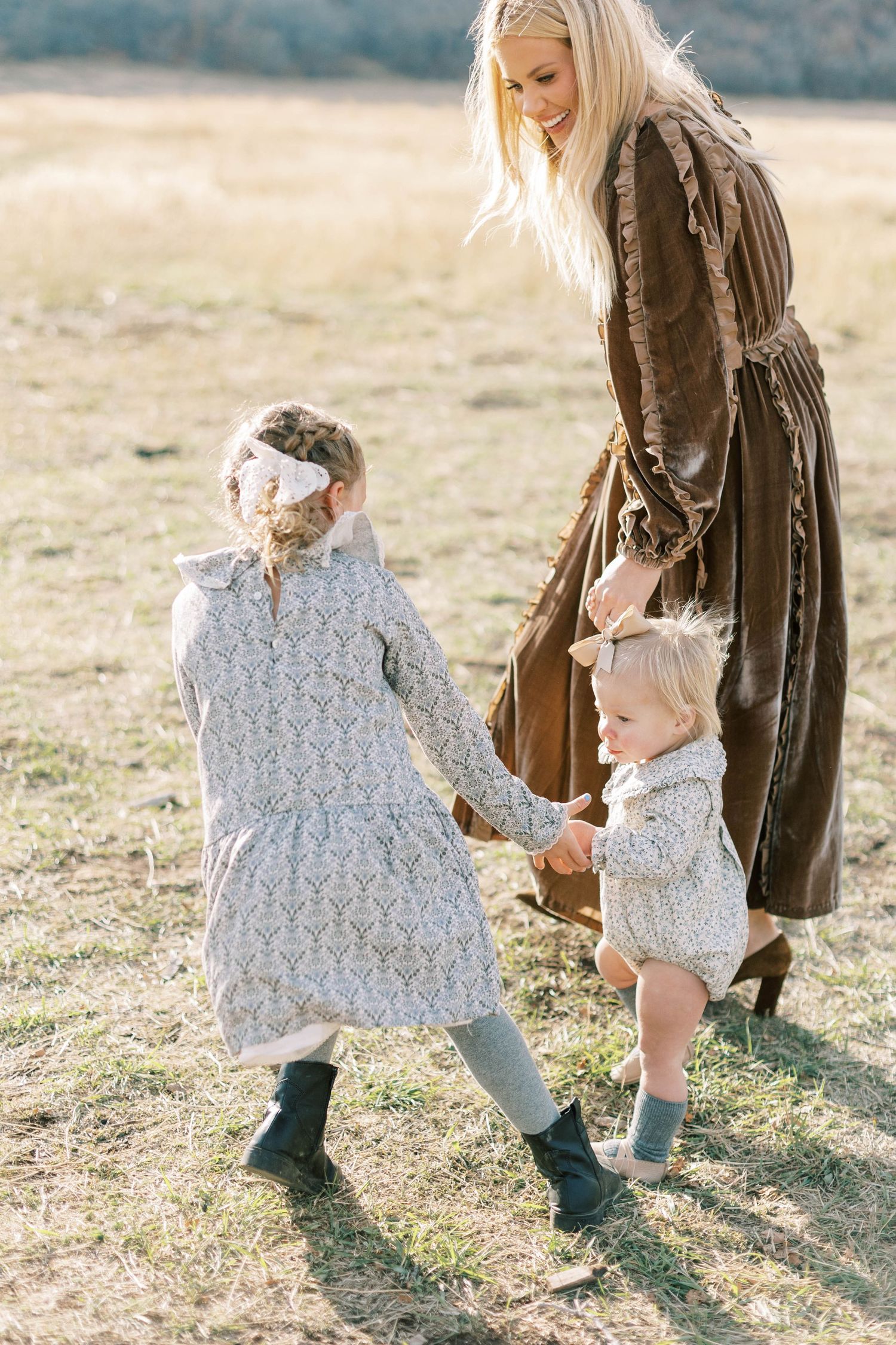 Family wears vintage inspired dresses while walking together in a sunlit mountain meadow.