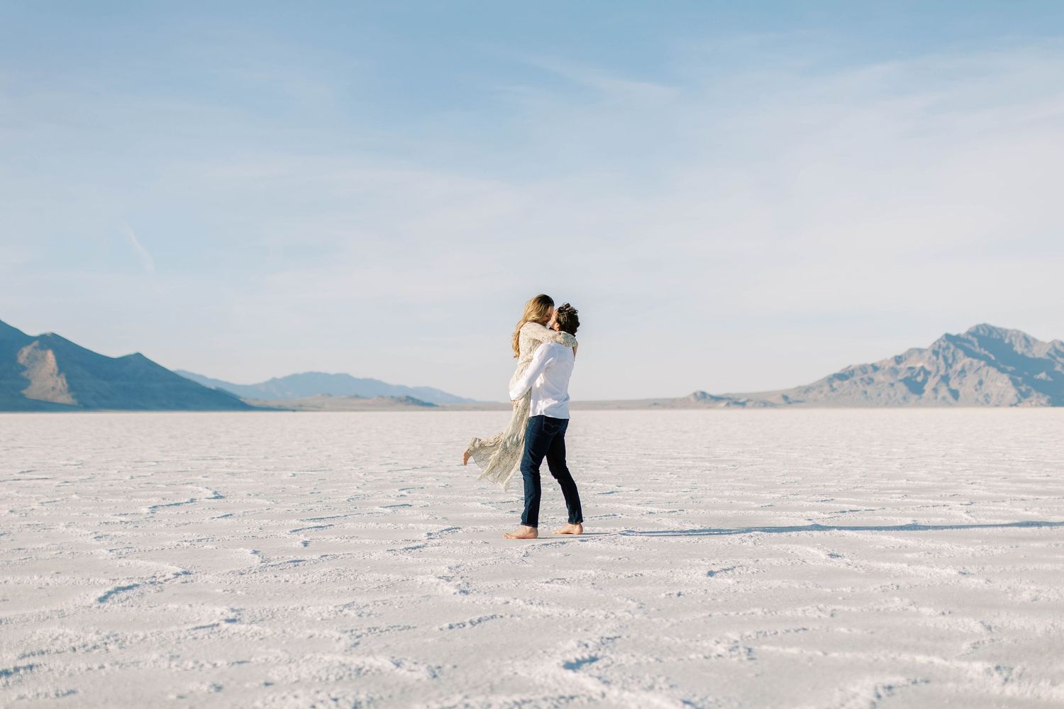 Two people dancing together on white salt flats with mountains visible in background.