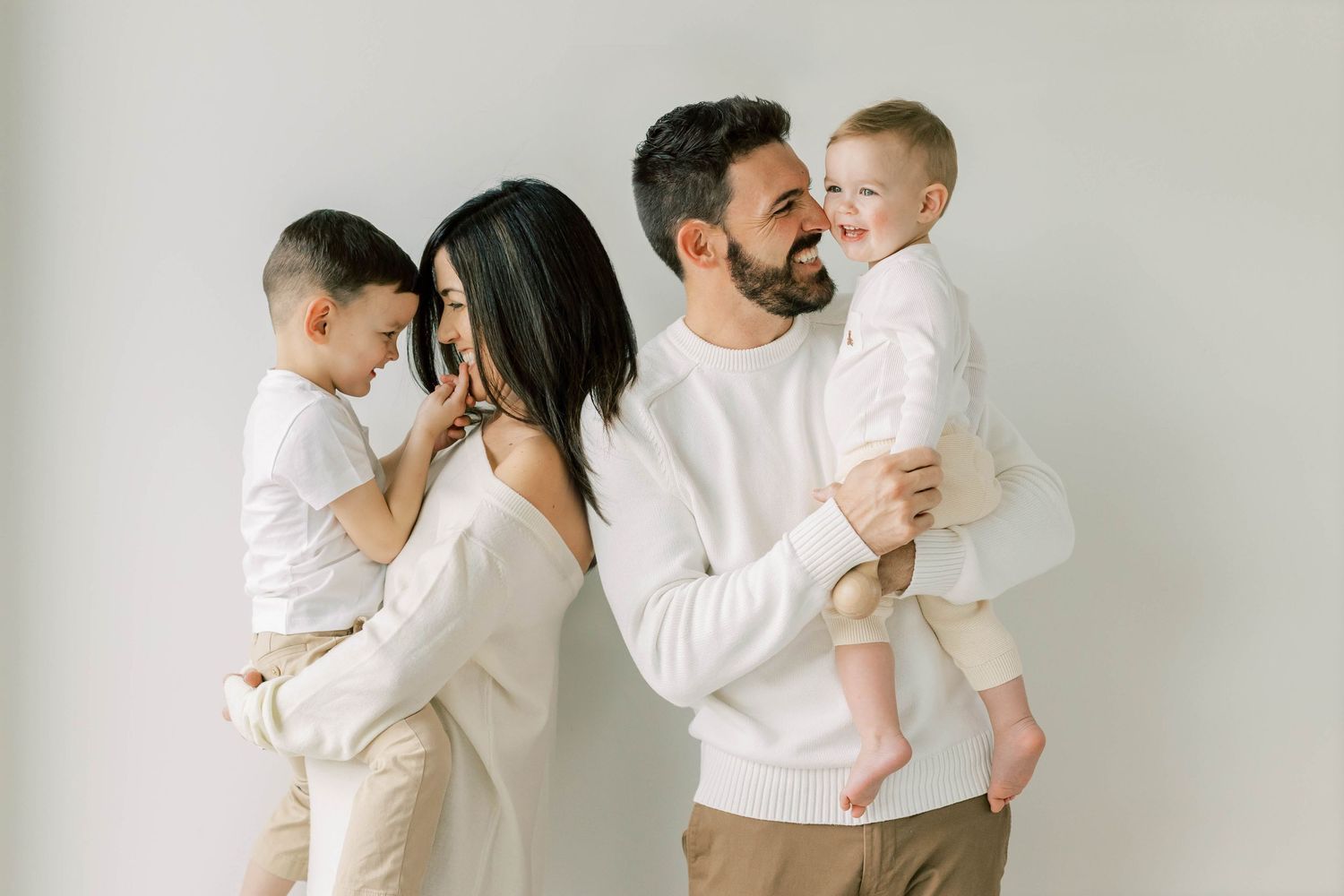 Family in matching white outfits share tender moment against neutral background.