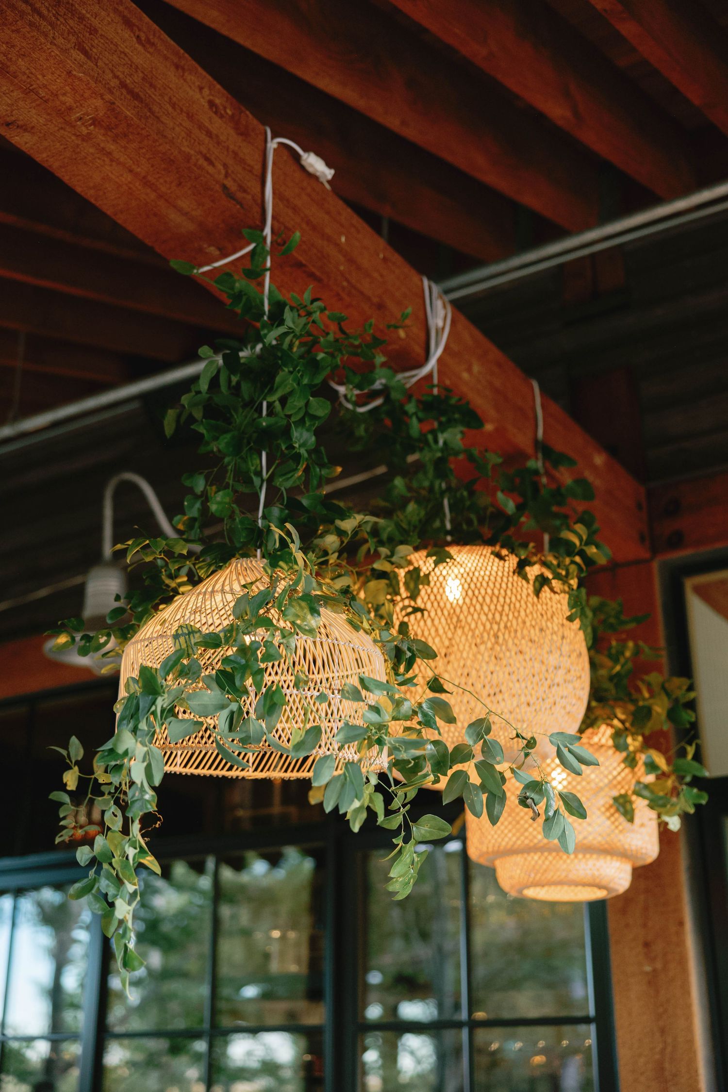 Woven basket pendant lights decorated with cascading greenery hang from wooden beams.