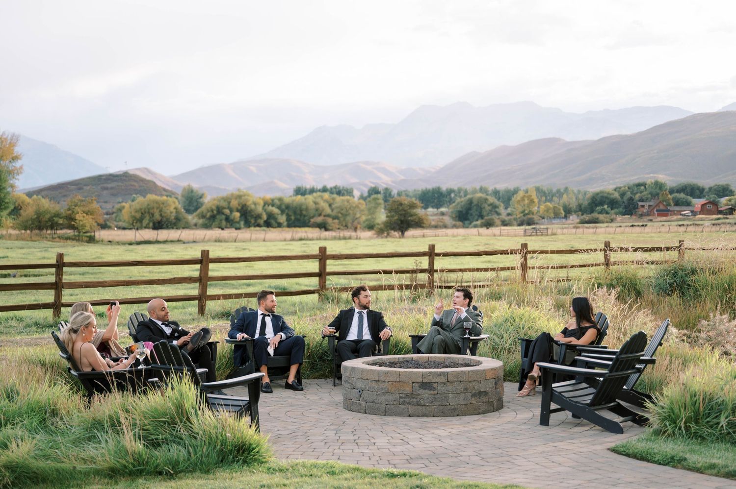 Wedding guests relax in Adirondack chairs overlooking a mountain landscape at an outdoor venue.
