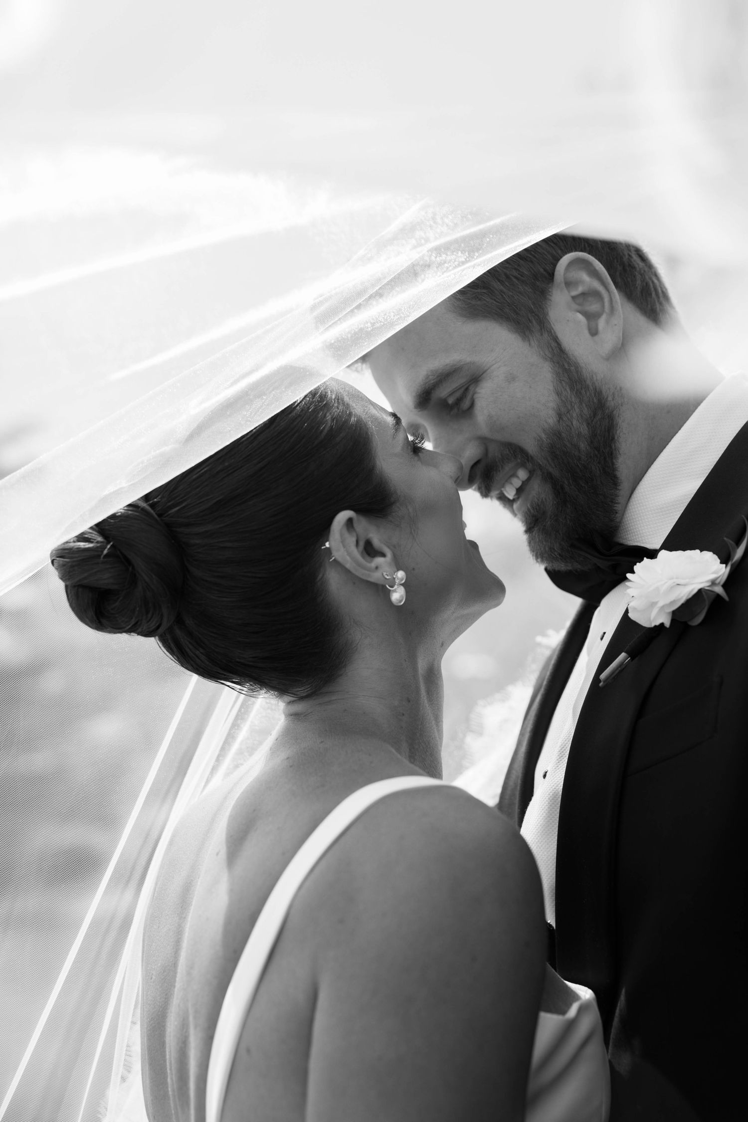 A romantic moment captured under a flowing veil in black and white.