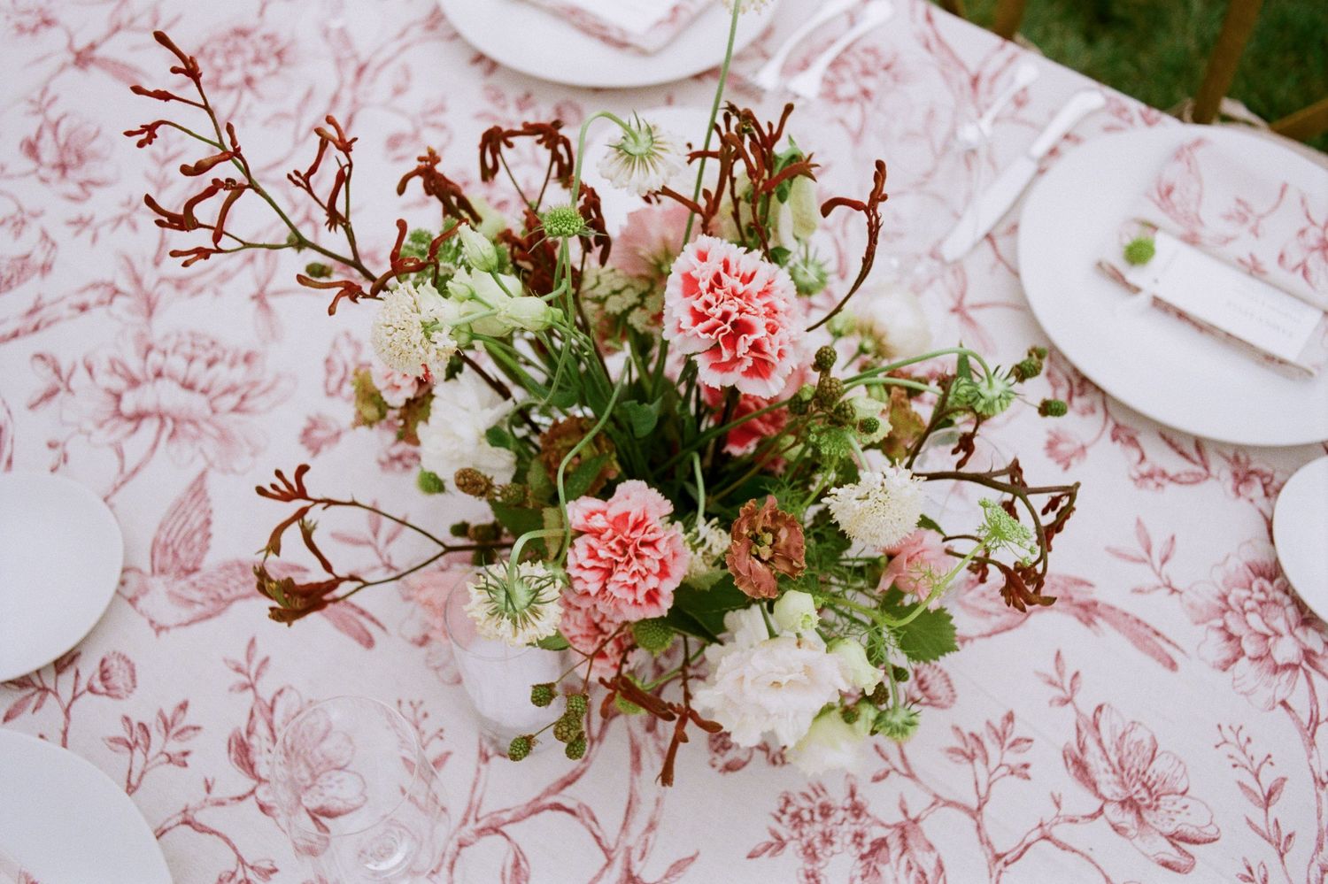 Delicate pink and white floral arrangement with carnations displayed on patterned tablecloth.
