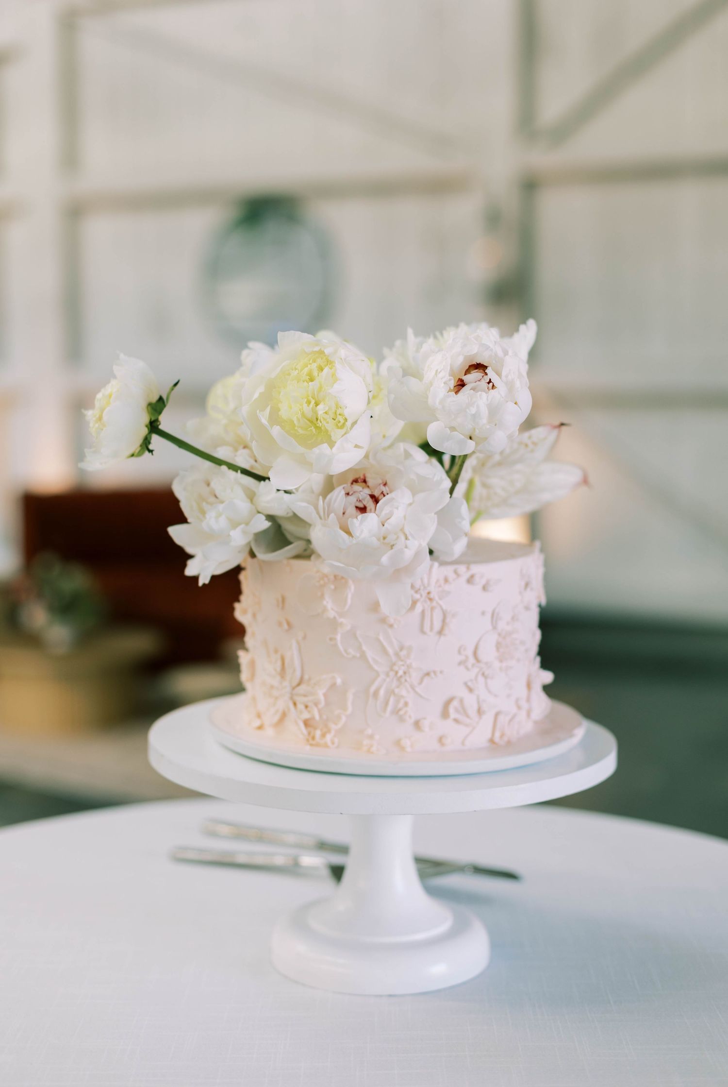 A delicate white wedding cake with floral decorations displayed on a white cake stand from multiple angles.
