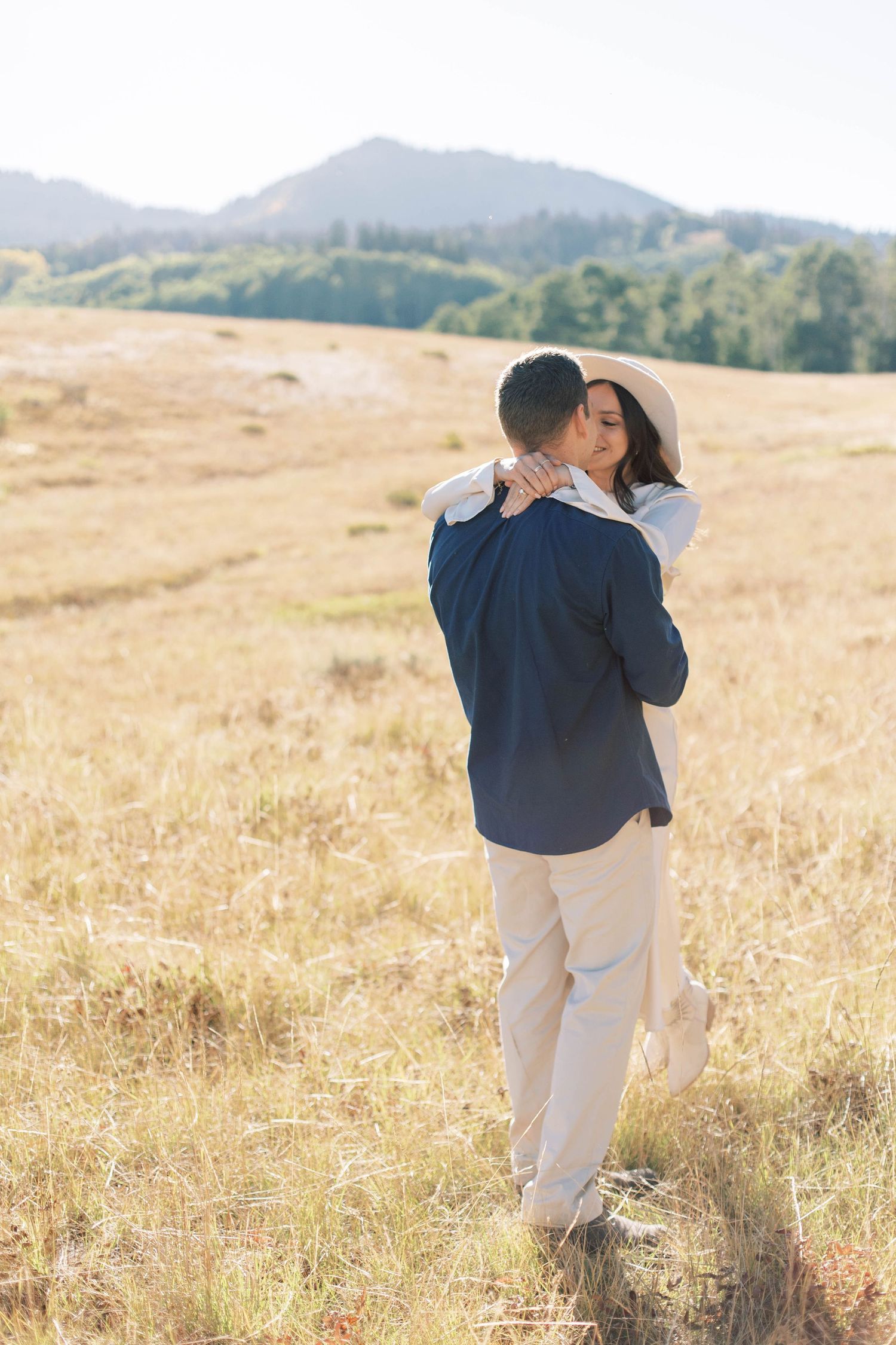 Romantic couple embracing in a sunlit mountain meadow wearing light colored clothing.