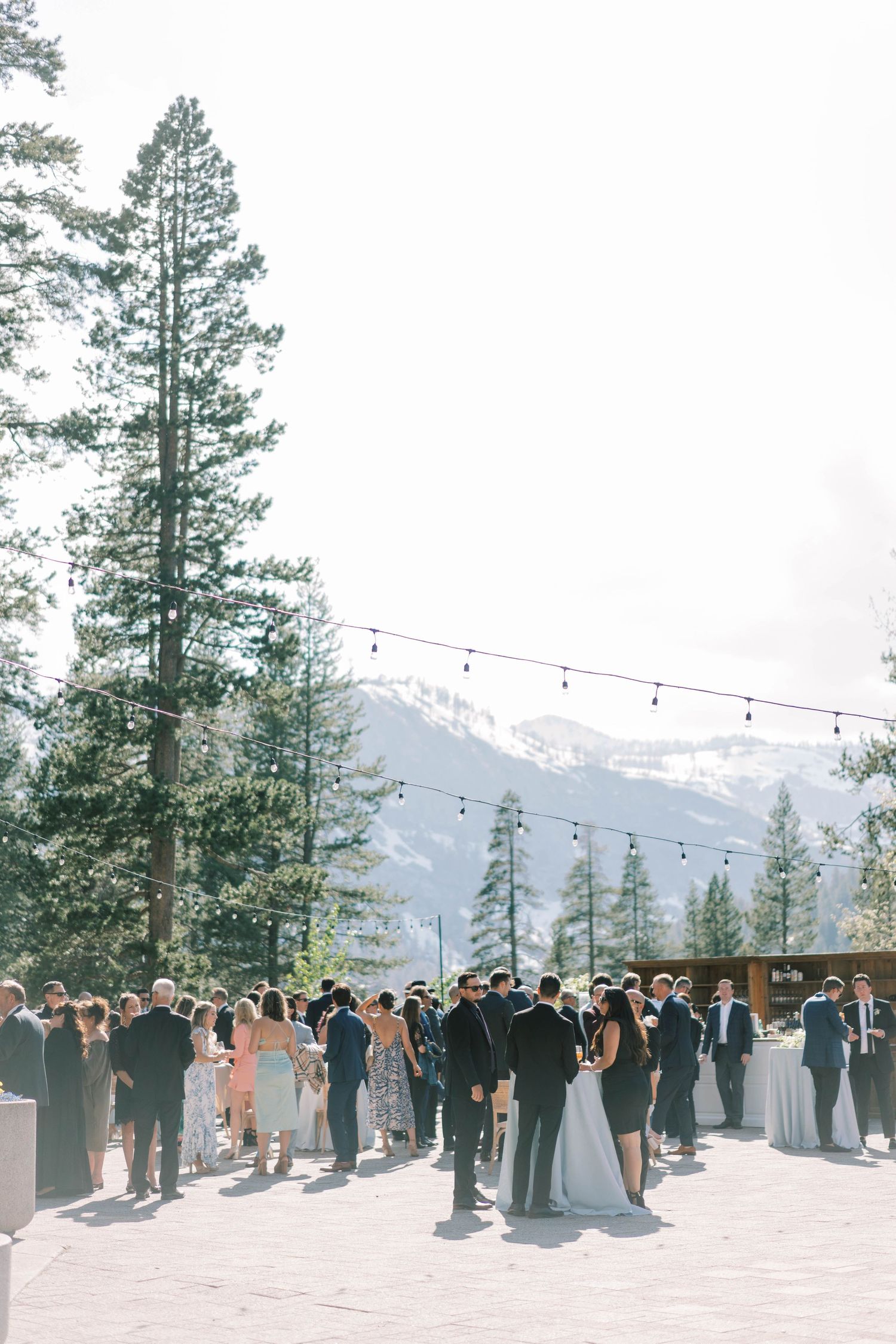 Wedding celebration gathering with mountain views and string lights at outdoor venue.