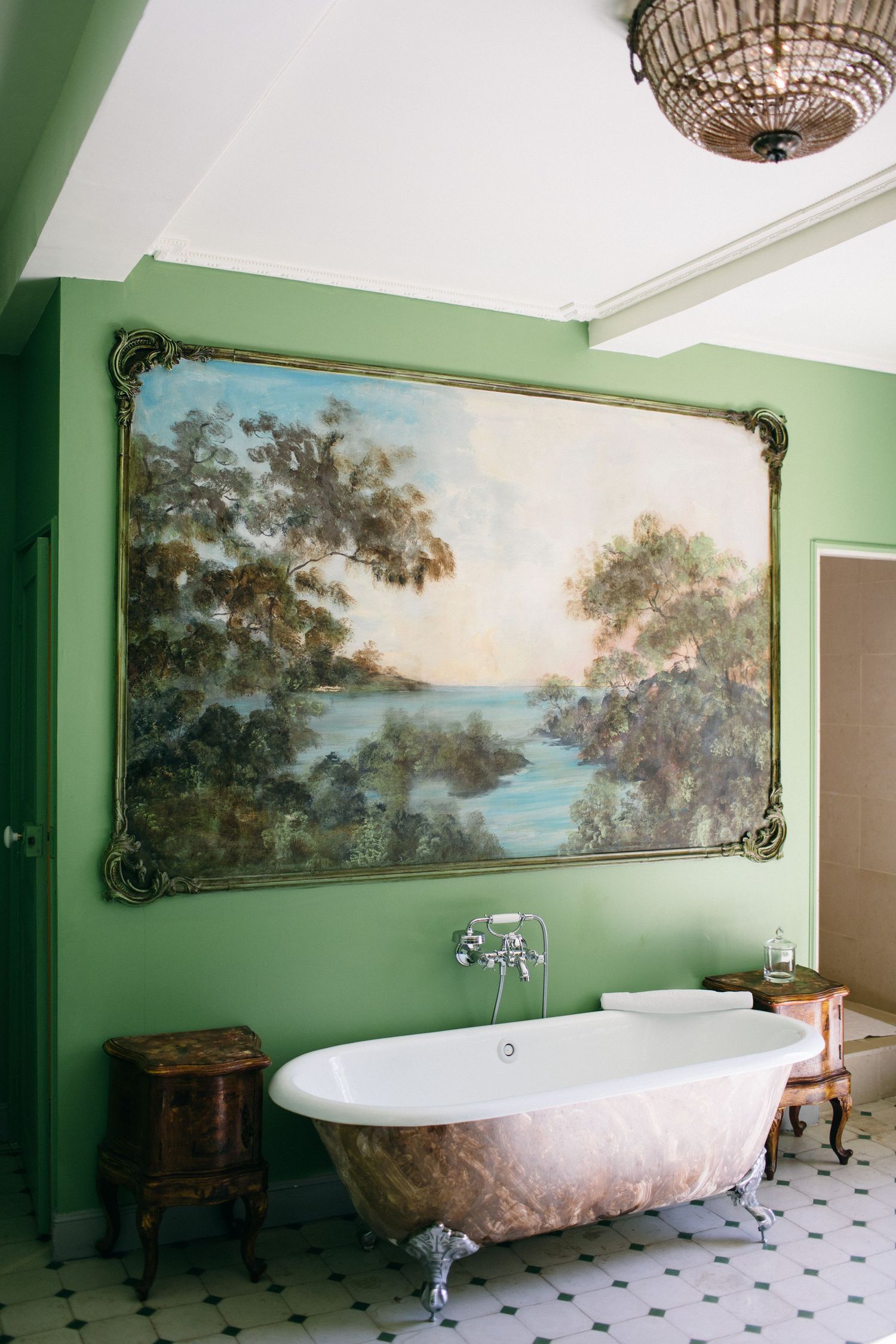 Luxury bathroom with clawfoot tub and large landscape painting on sage green walls.