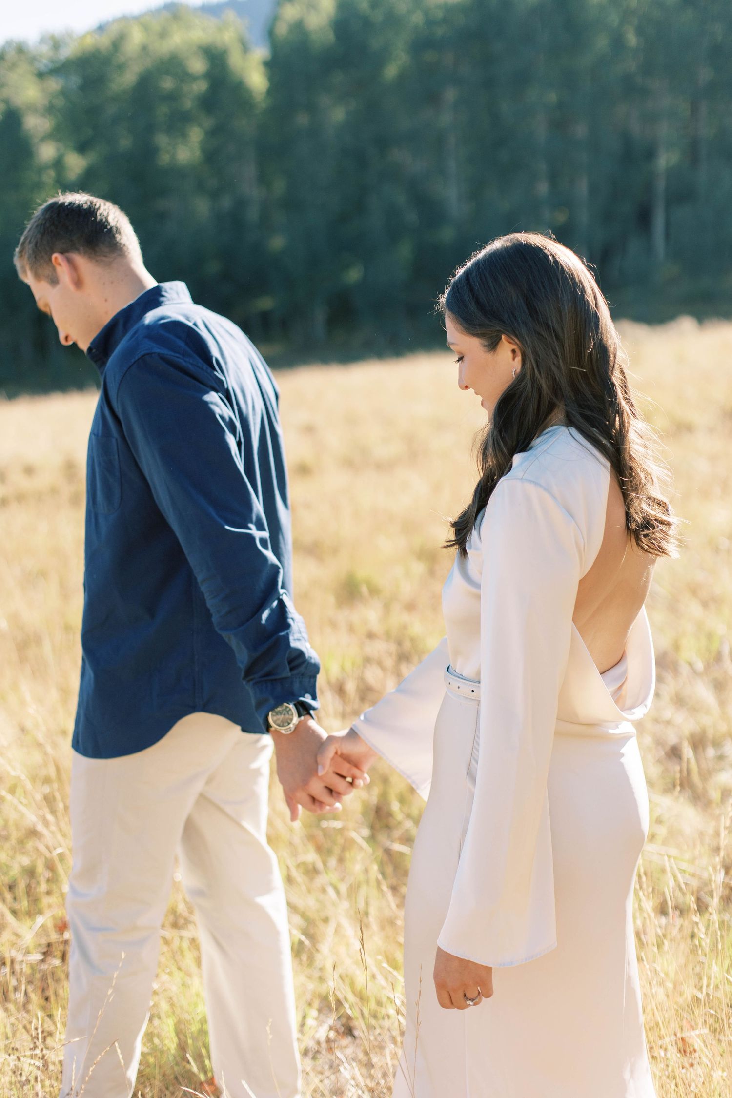 Couple in white and navy outfits holding hands in a sunlit meadow.