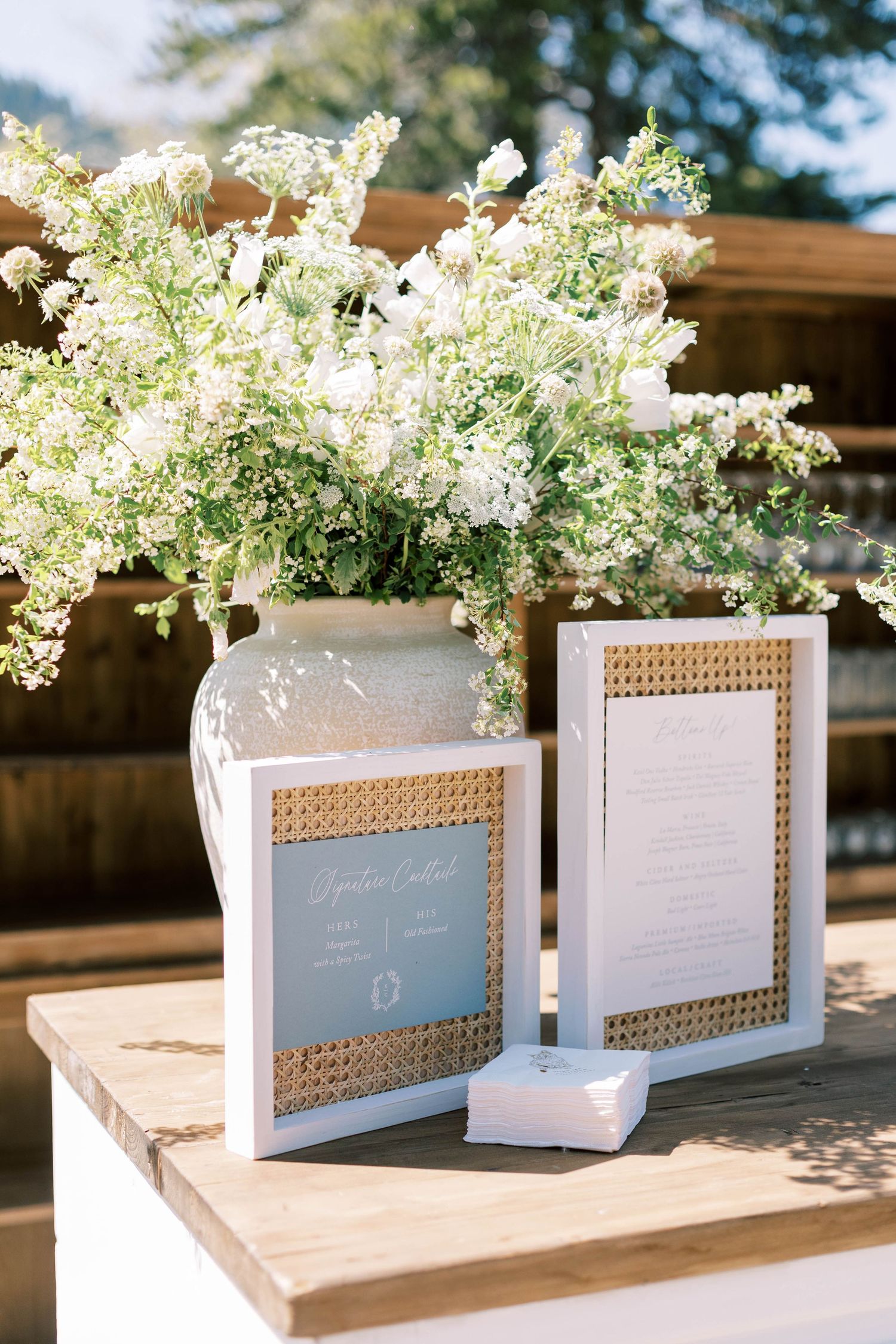 Wedding stationery displayed with white floral arrangement and rattan-framed menus.