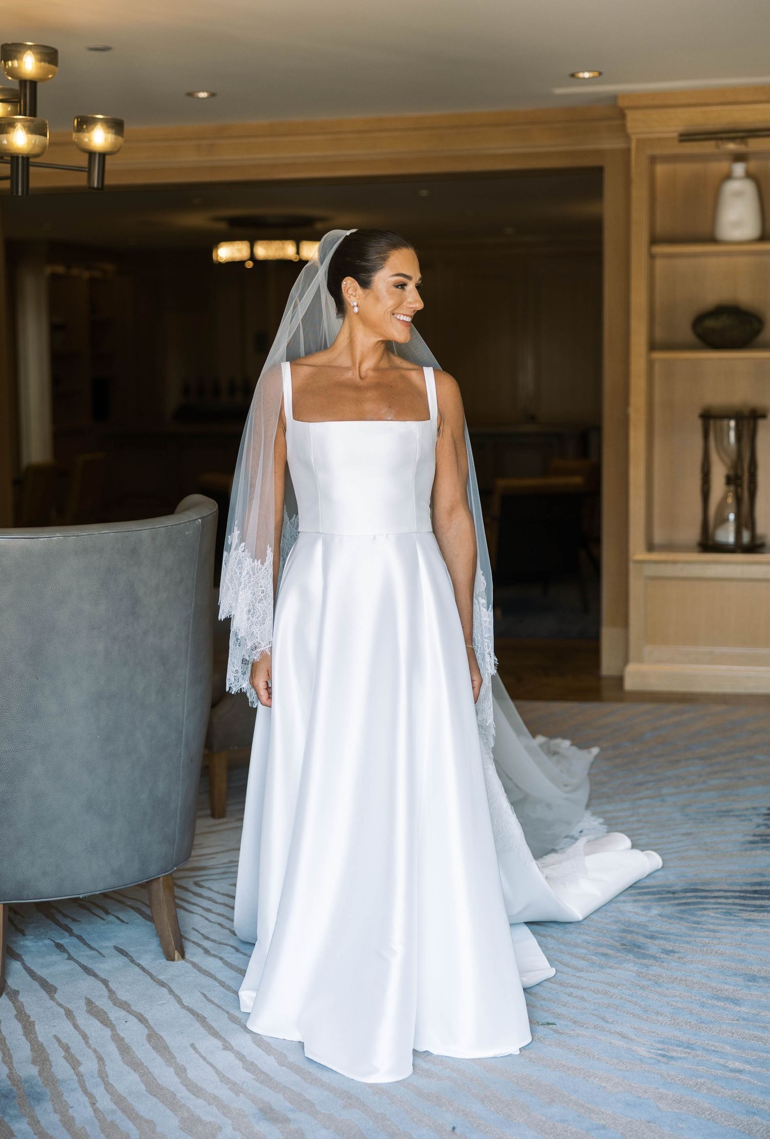 A bride in a white wedding gown and veil poses gracefully in a luxurious indoor setting with warm lighting.