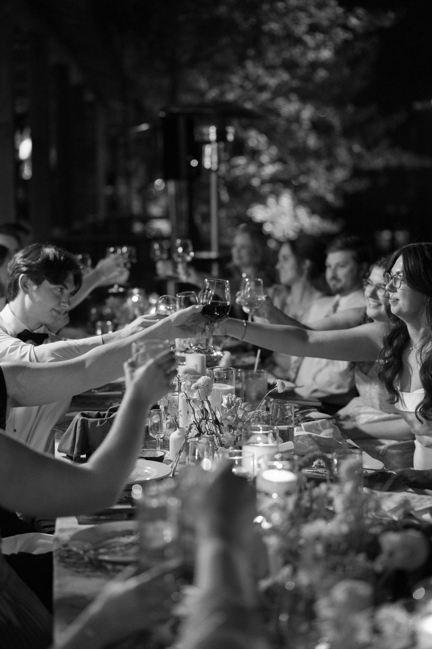 Wedding guests raise glasses in a toast during an evening reception dinner.