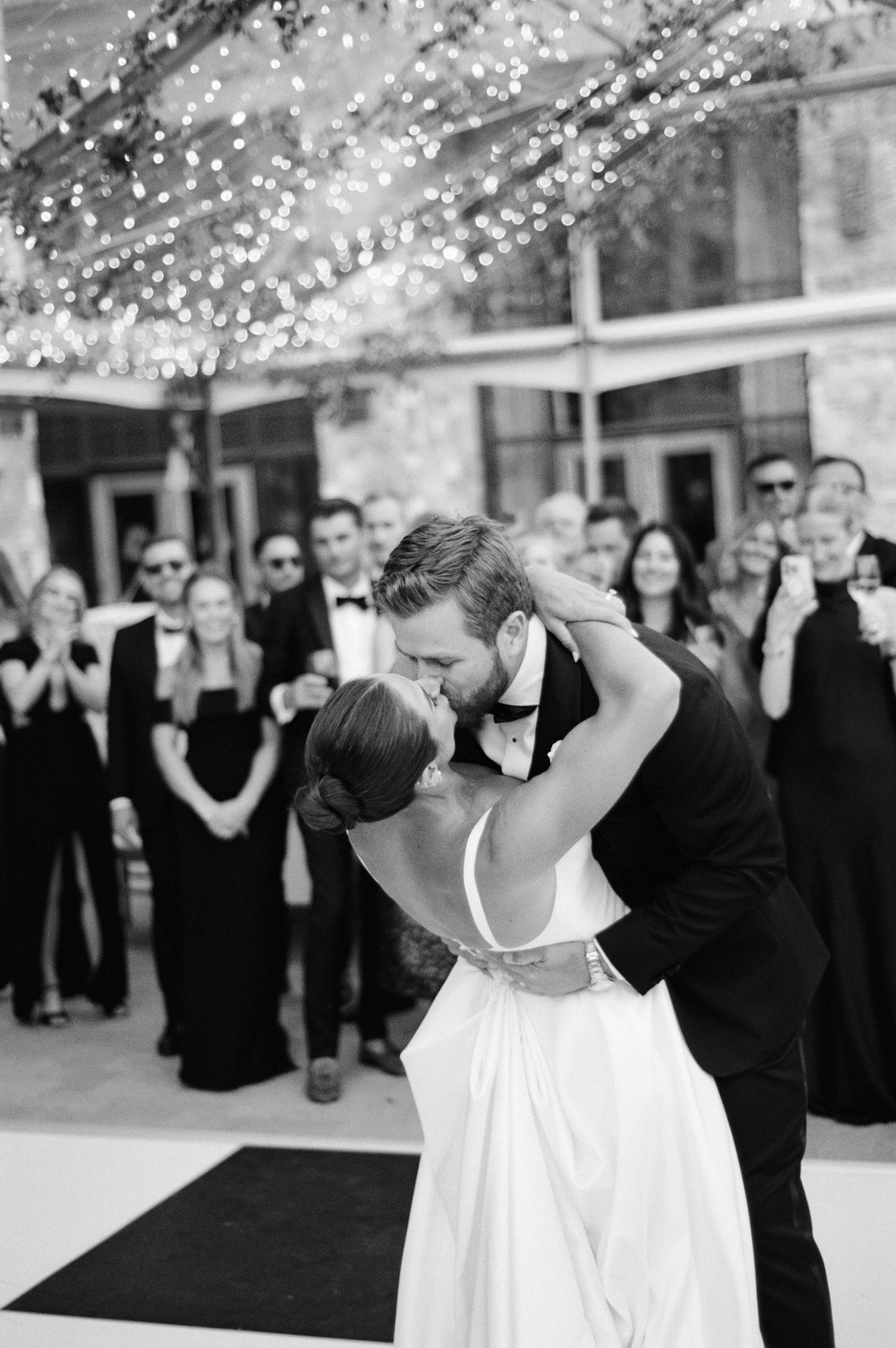 Black and white wedding dance sequence showing couple twirling and dipping on dance floor surrounded by guests.