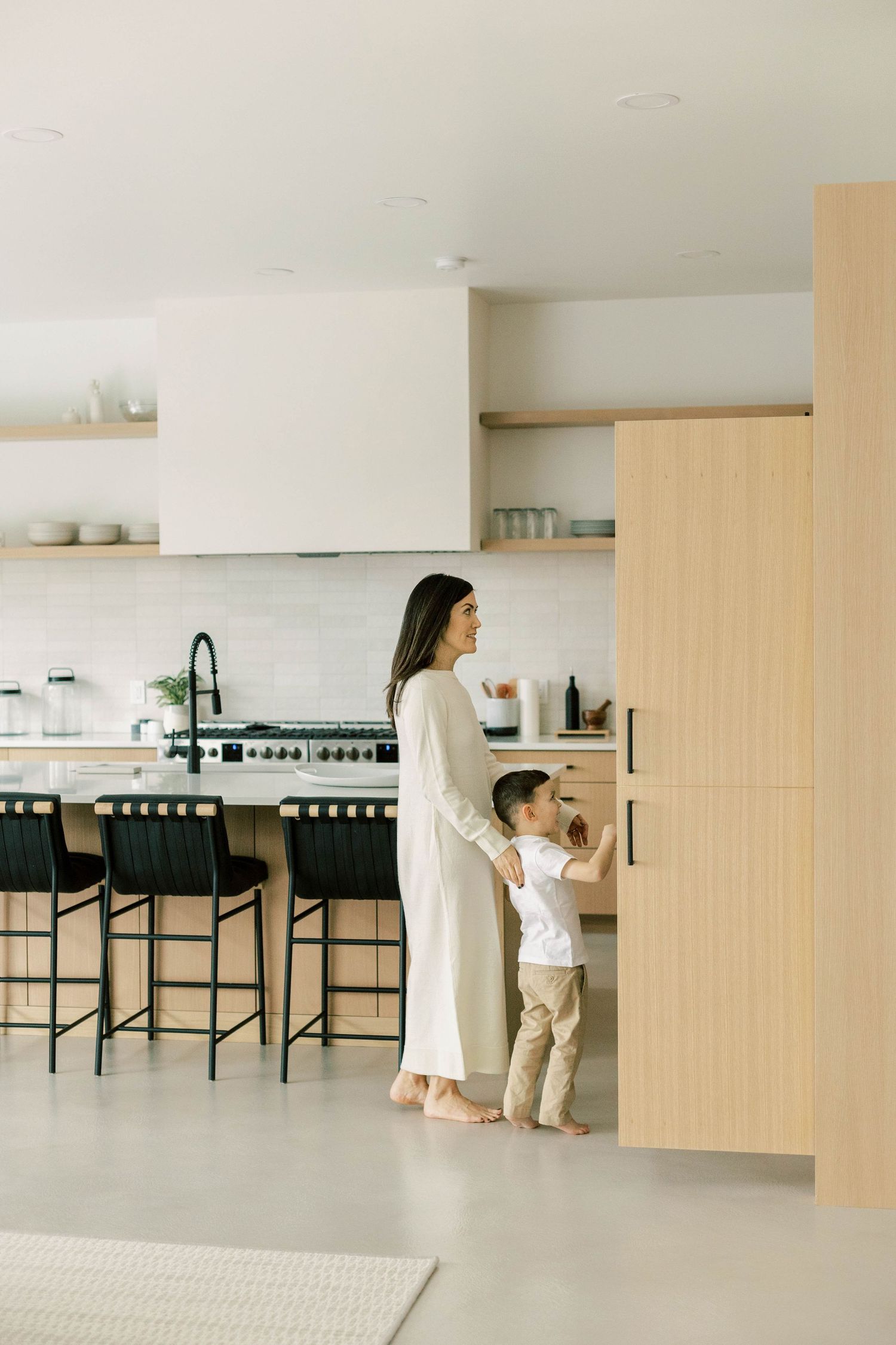Parent and child standing together in sleek modern kitchen with white and wood design elements.
