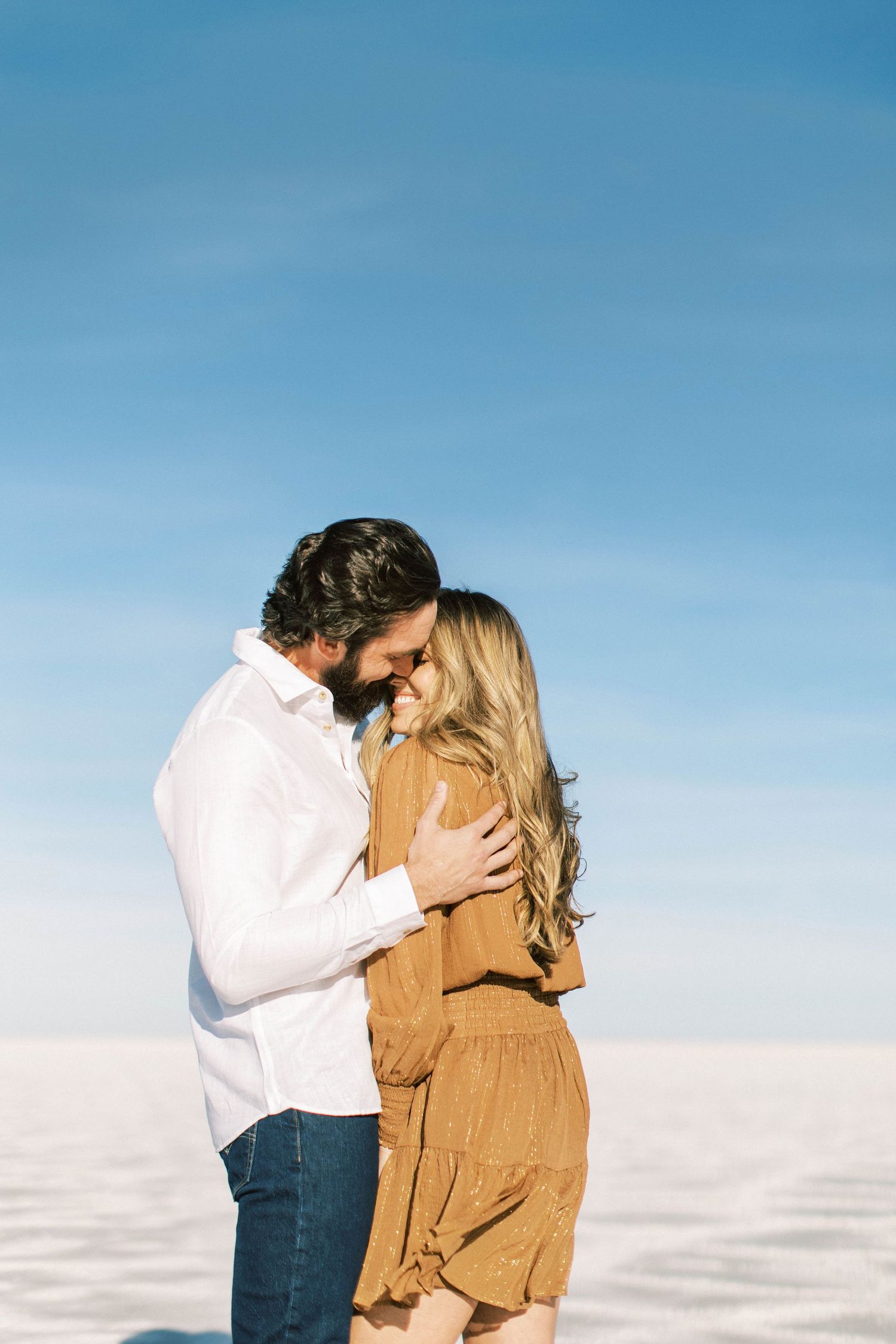 Intimate embrace captured against bright blue sky on white salt flats.