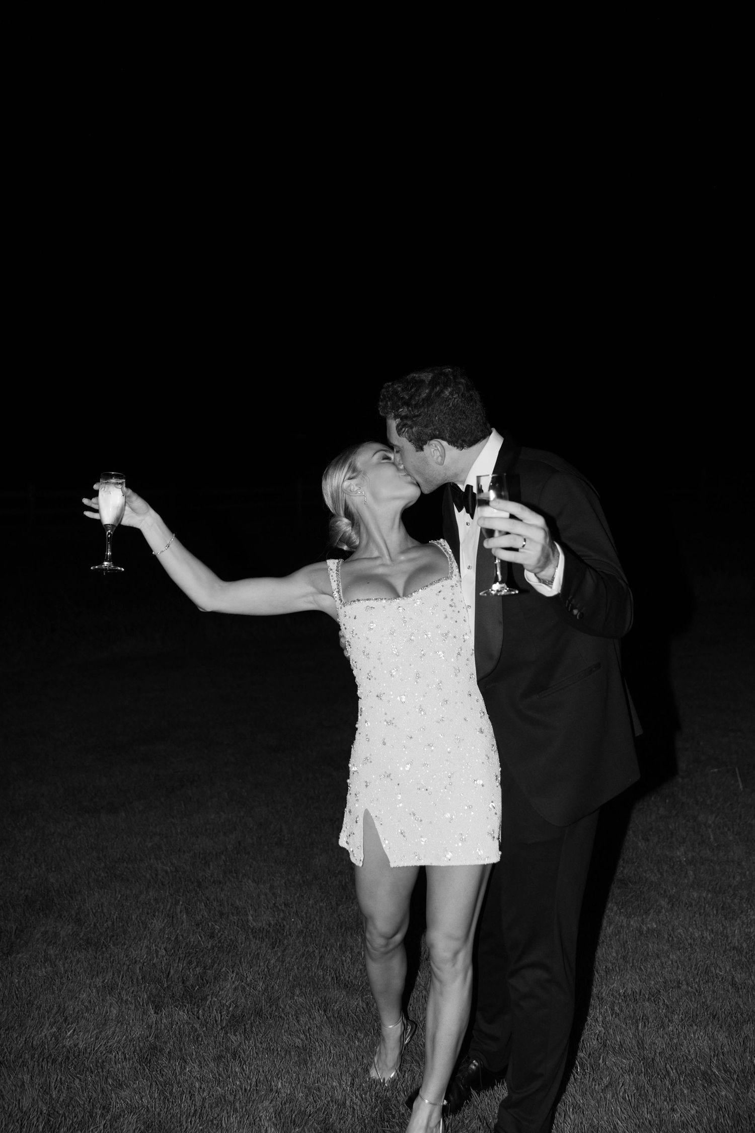 Couple dancing with champagne glasses at night in formal attire.