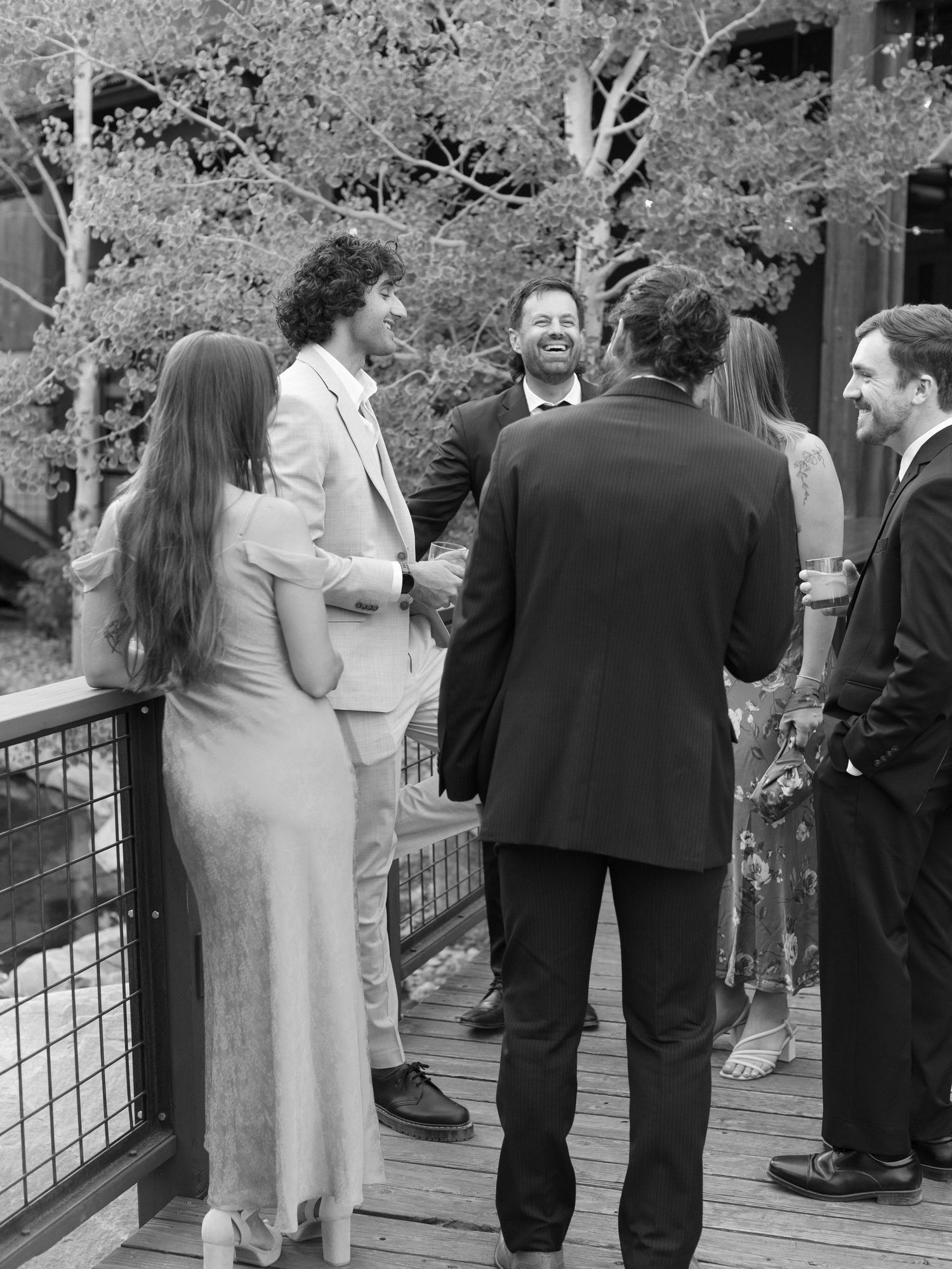 Wedding guests gathered on an outdoor deck surrounded by trees in black and white.