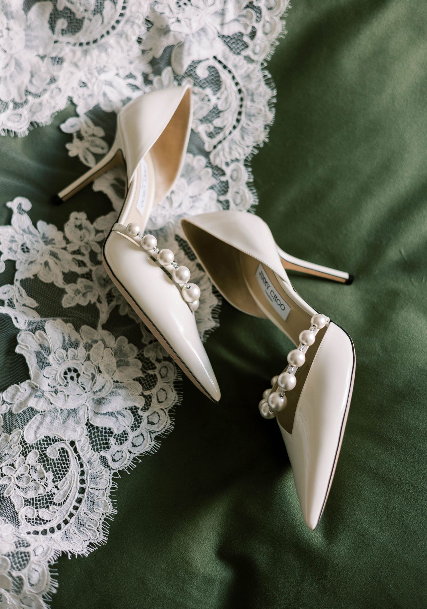 White bridal stiletto heels arranged on delicate white lace against an emerald green background.