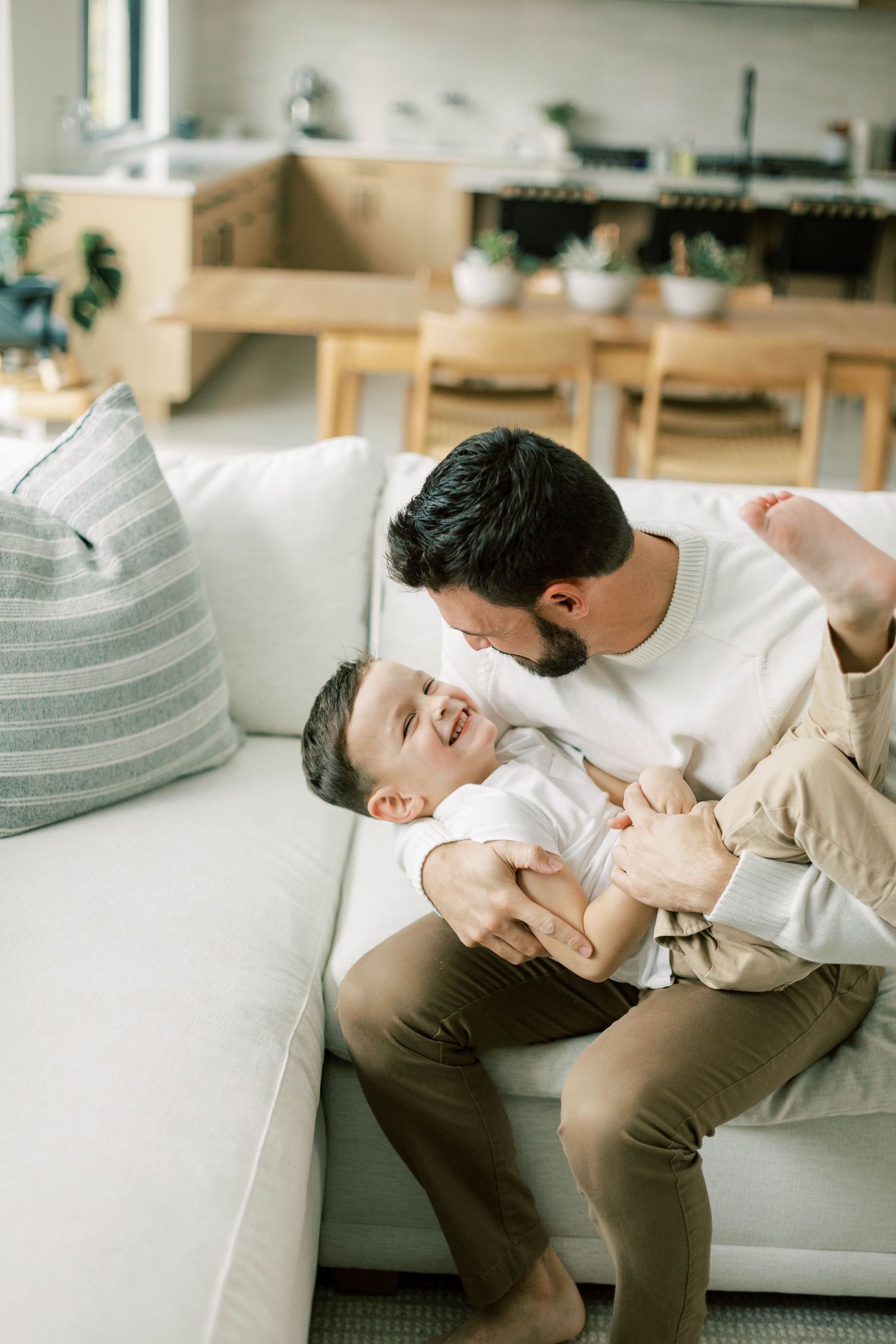 Tender moment between parent and child on white couch in modern living room.