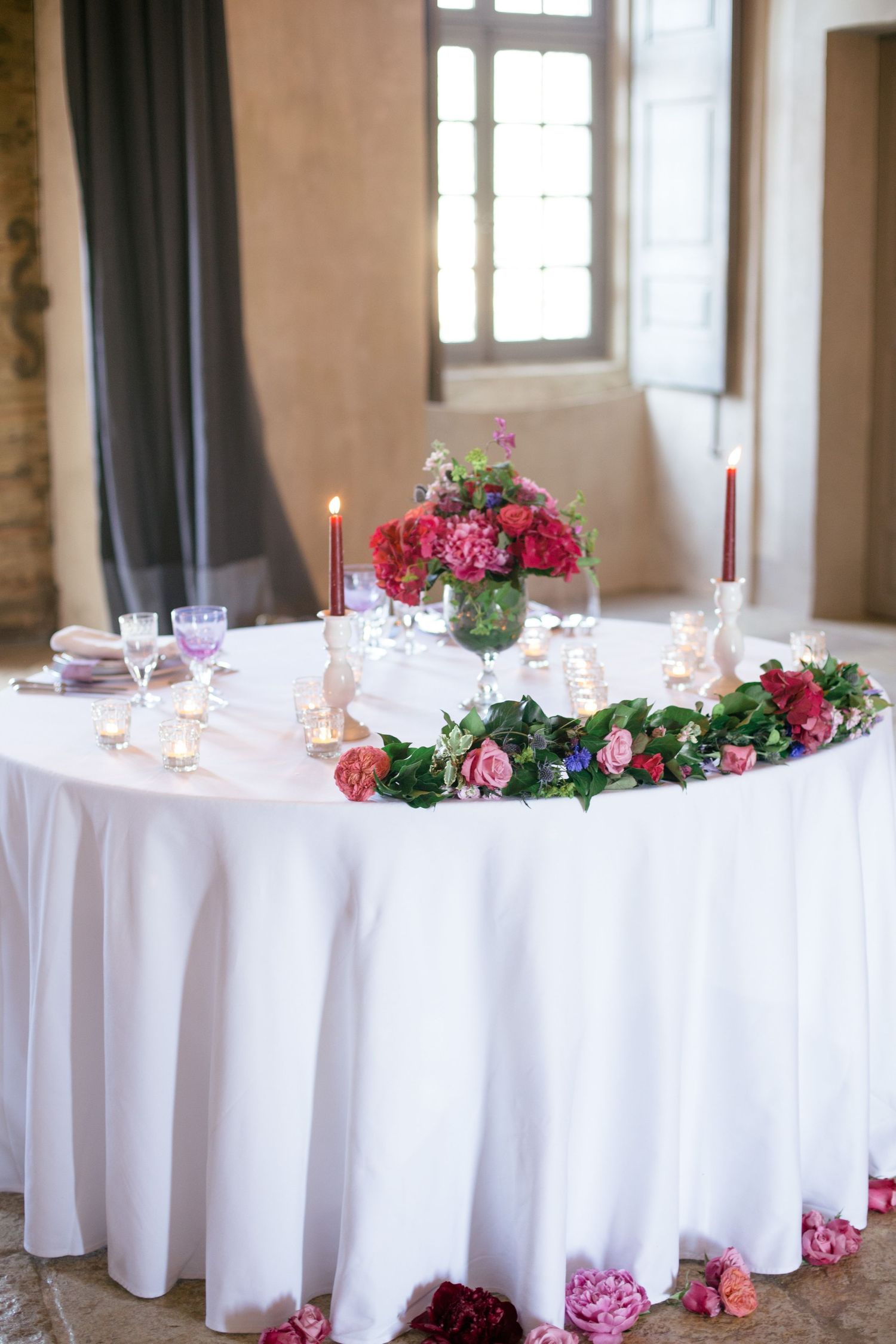 Elegant round table with white tablecloth decorated with pink roses and place settings.