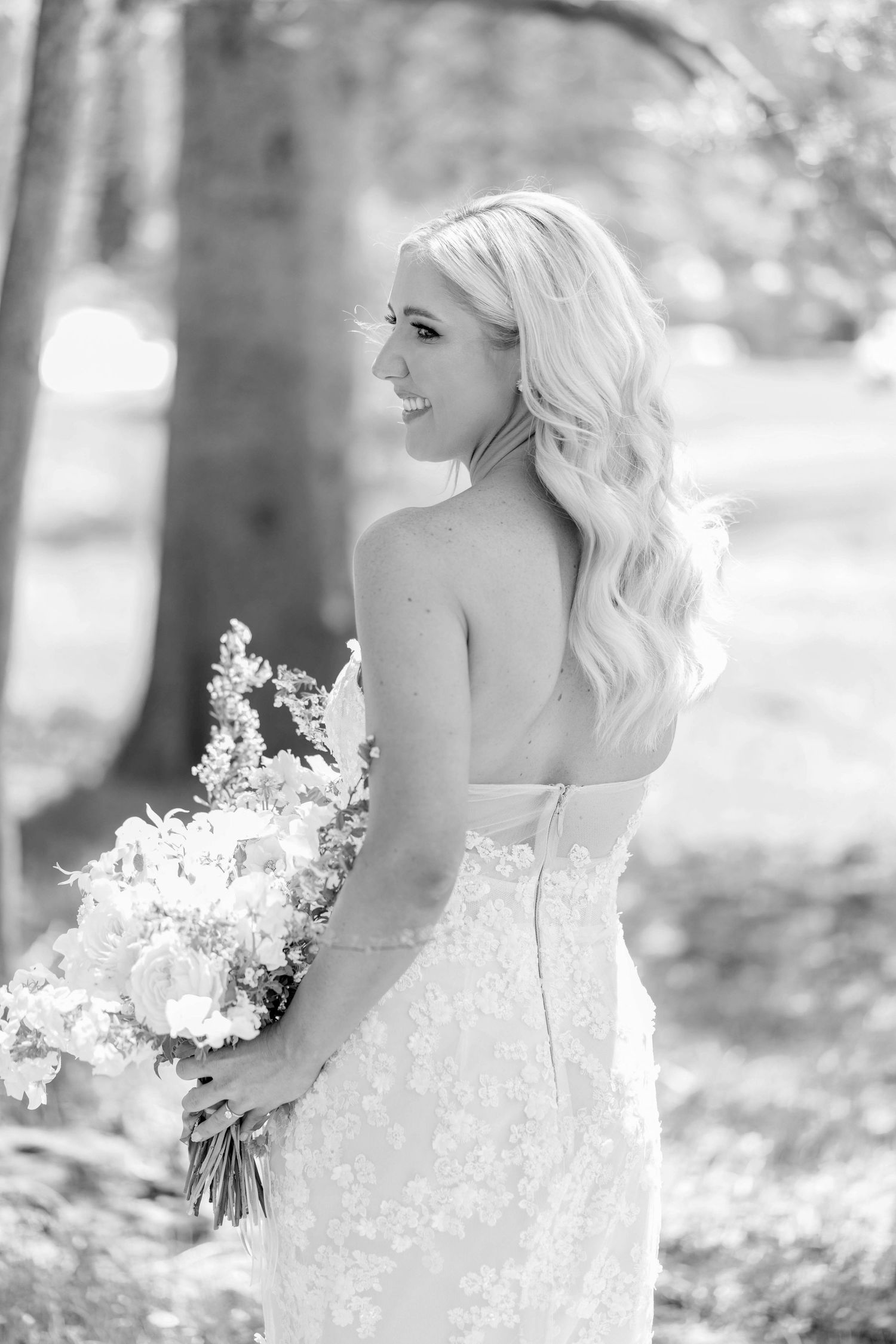 A close-up black and white portrait showcasing a delicate lace wedding dress and floral bouquet.