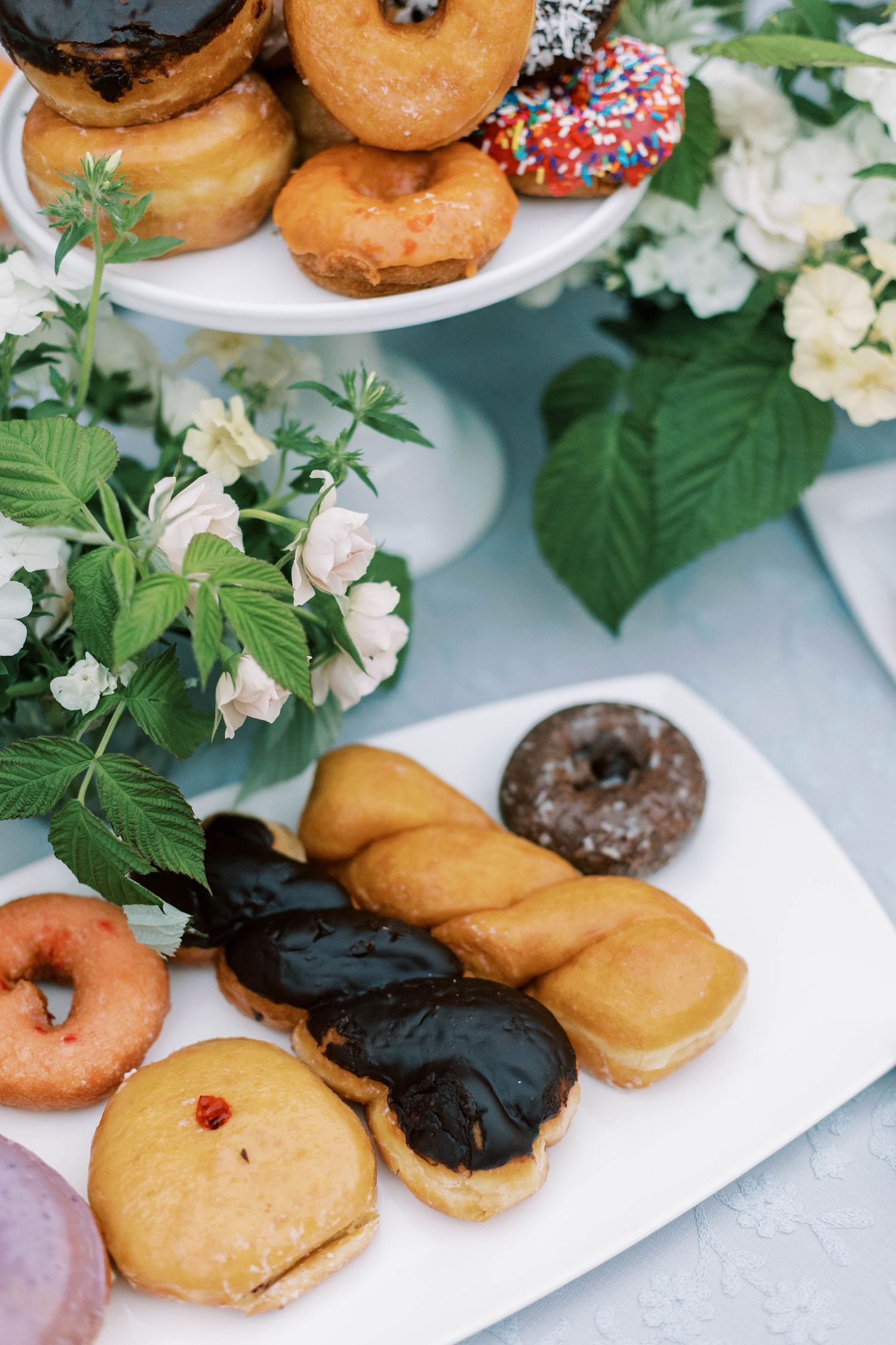 Assorted donuts and delicate floral arrangements on white serving plates.