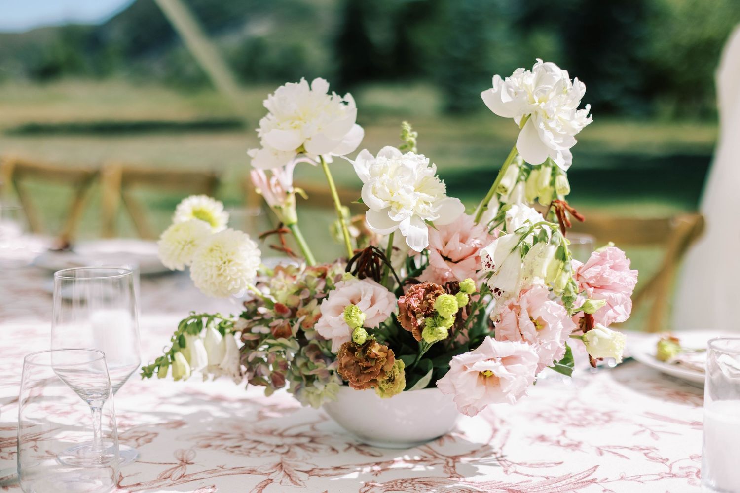 Elegant floral centerpieces with white and pink blooms line a wedding reception table with delicate table settings.
