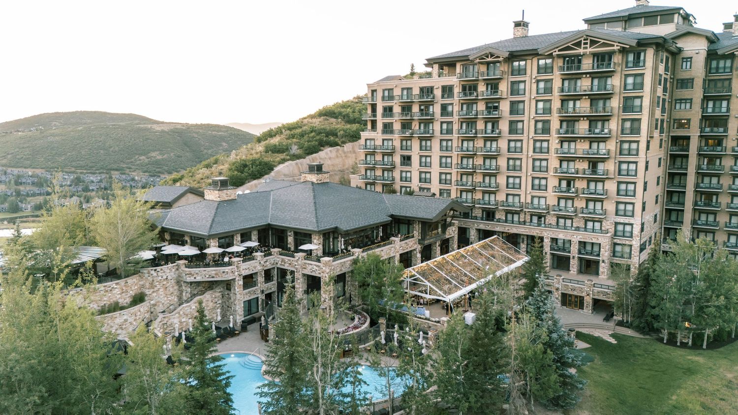 A panoramic view of a mountain resort complex with multiple buildings, swimming pools and surrounding green landscape.