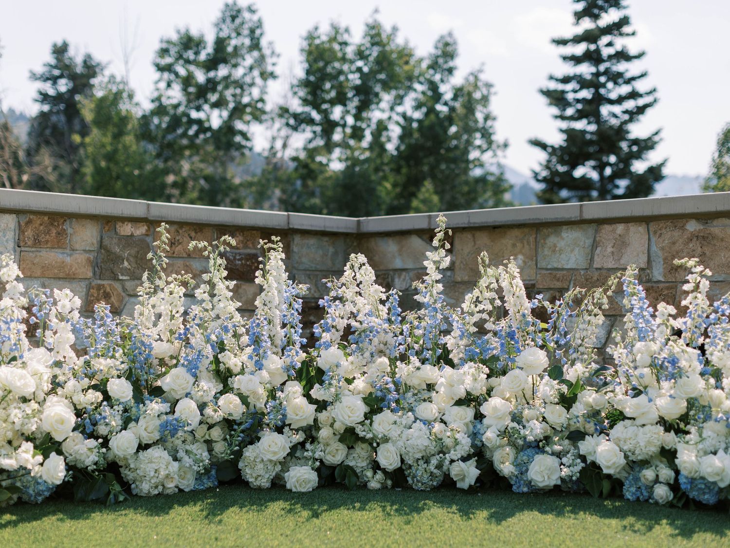 A stunning floral arch installation with white roses and greenery creates an elegant outdoor wedding ceremony backdrop.
