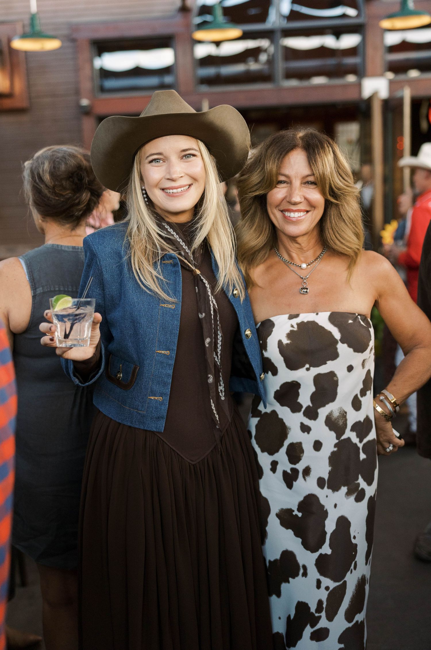 Two people wearing western style outfits with cowboy hats pose together at a casual gathering.