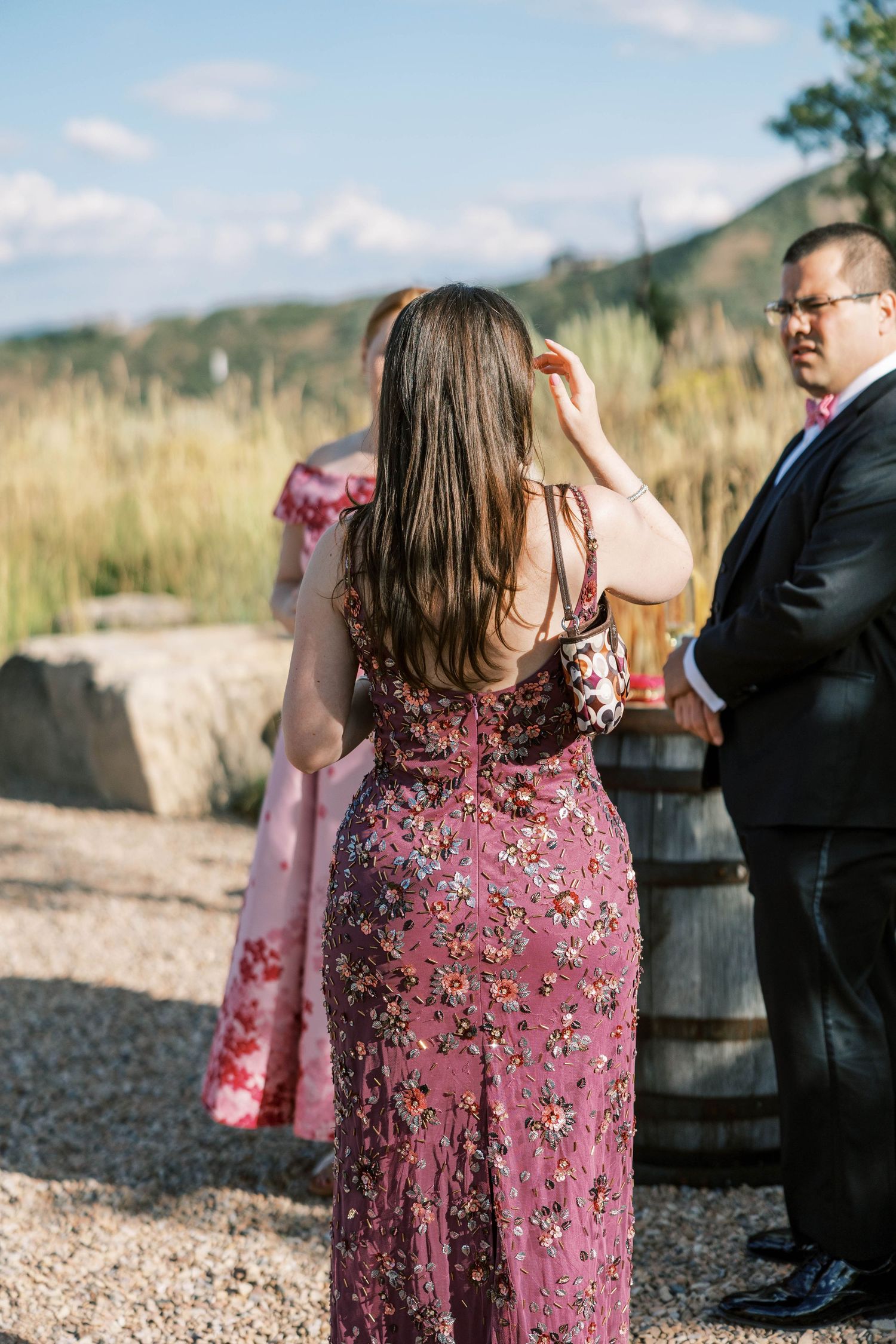 Wedding guests in floral dresses gathered outdoors at rustic mountain venue.
