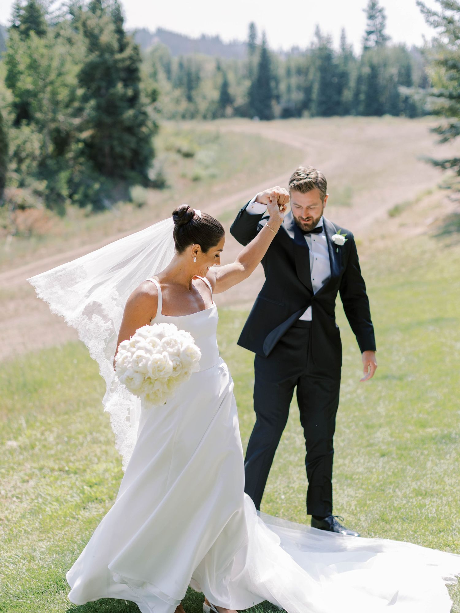 Wedding couple walking on a grassy hillside with evergreen trees in the mountain landscape.