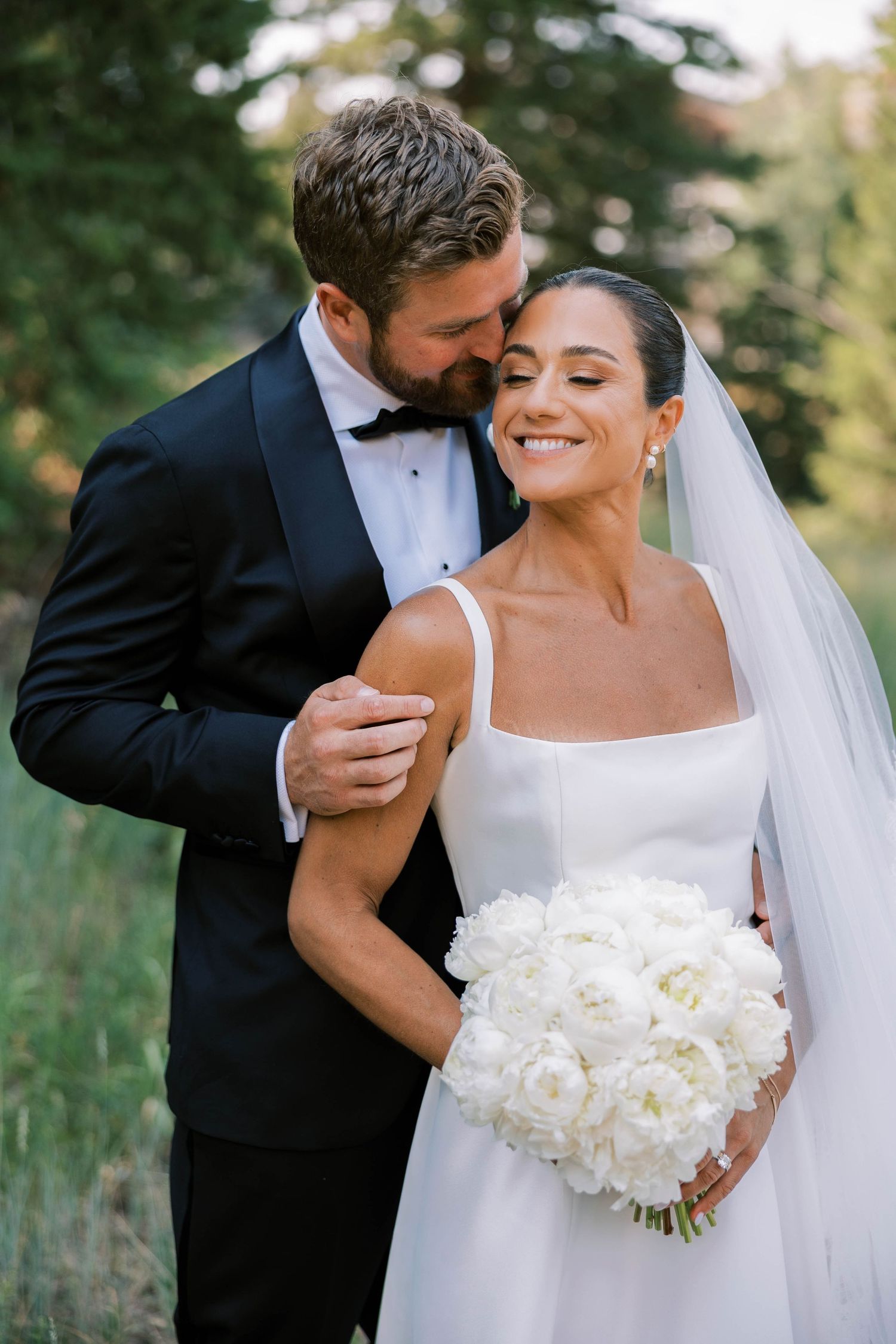 Romantic wedding couple shares intimate moments in a garden setting with a stunning white floral bouquet.