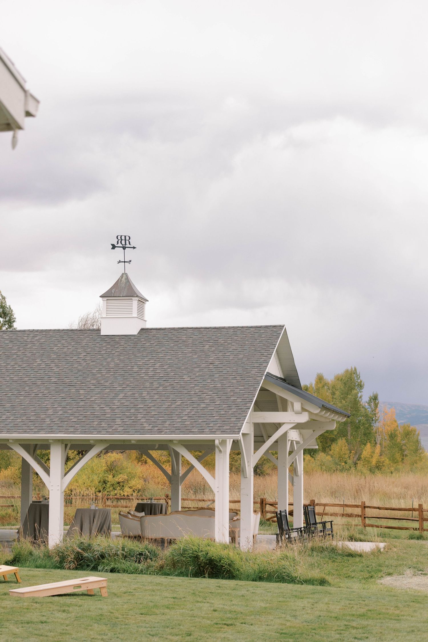White wooden gazebos stand in a row on grassy terrain with autumn foliage and cloudy skies in the background.