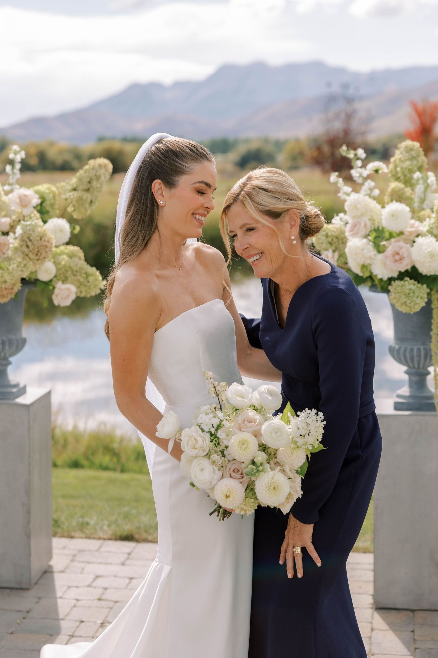 Emotional wedding moment captured outdoors with white floral arrangements and mountain backdrop.
