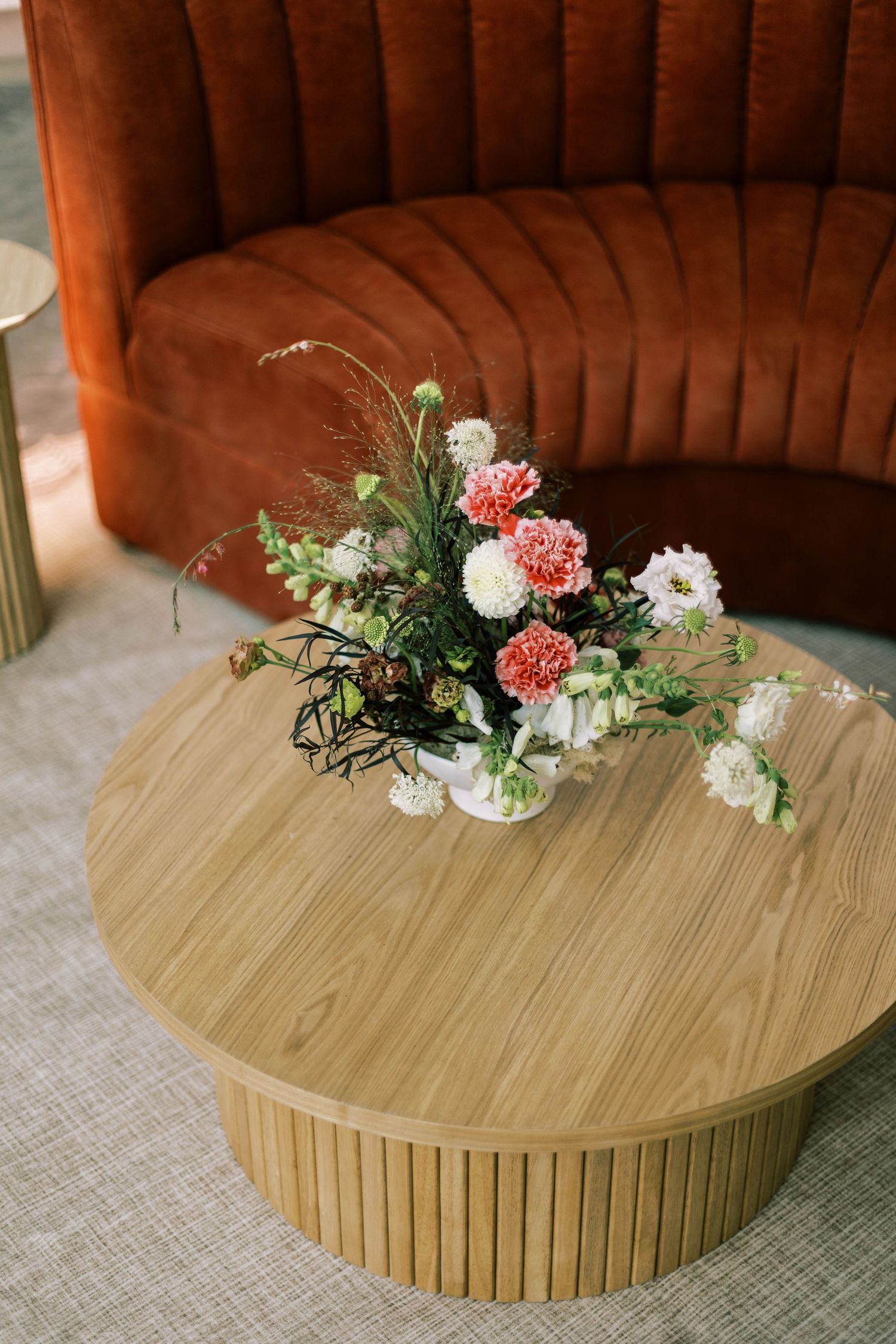 A round wooden coffee table decorated with pink and white floral arrangements and greenery on a textured rug.
