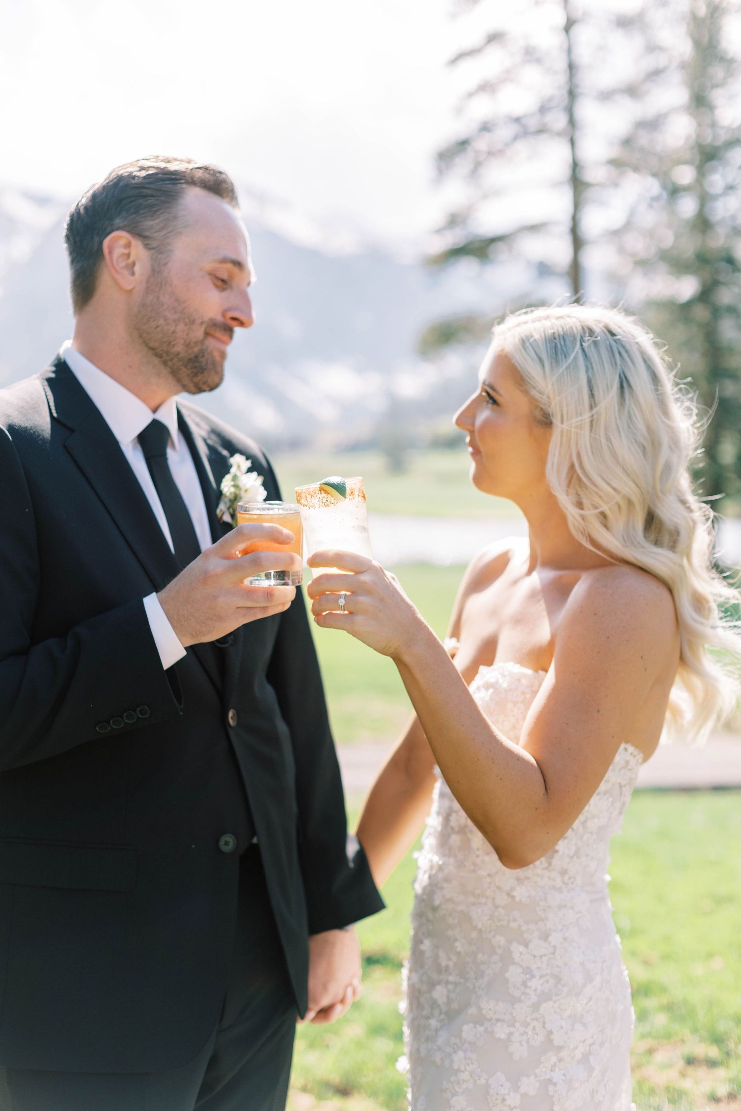 Couple shares drinks during wedding celebration with mountain backdrop.