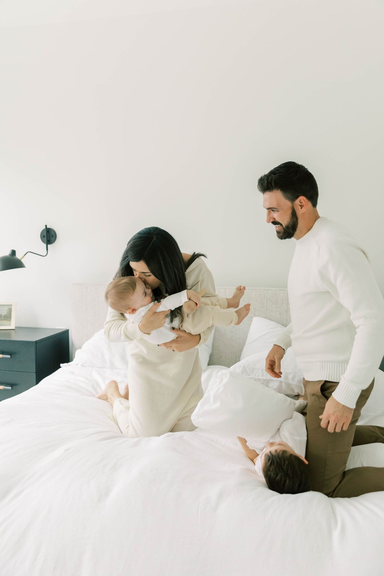 Family enjoying casual morning together on white bedding.