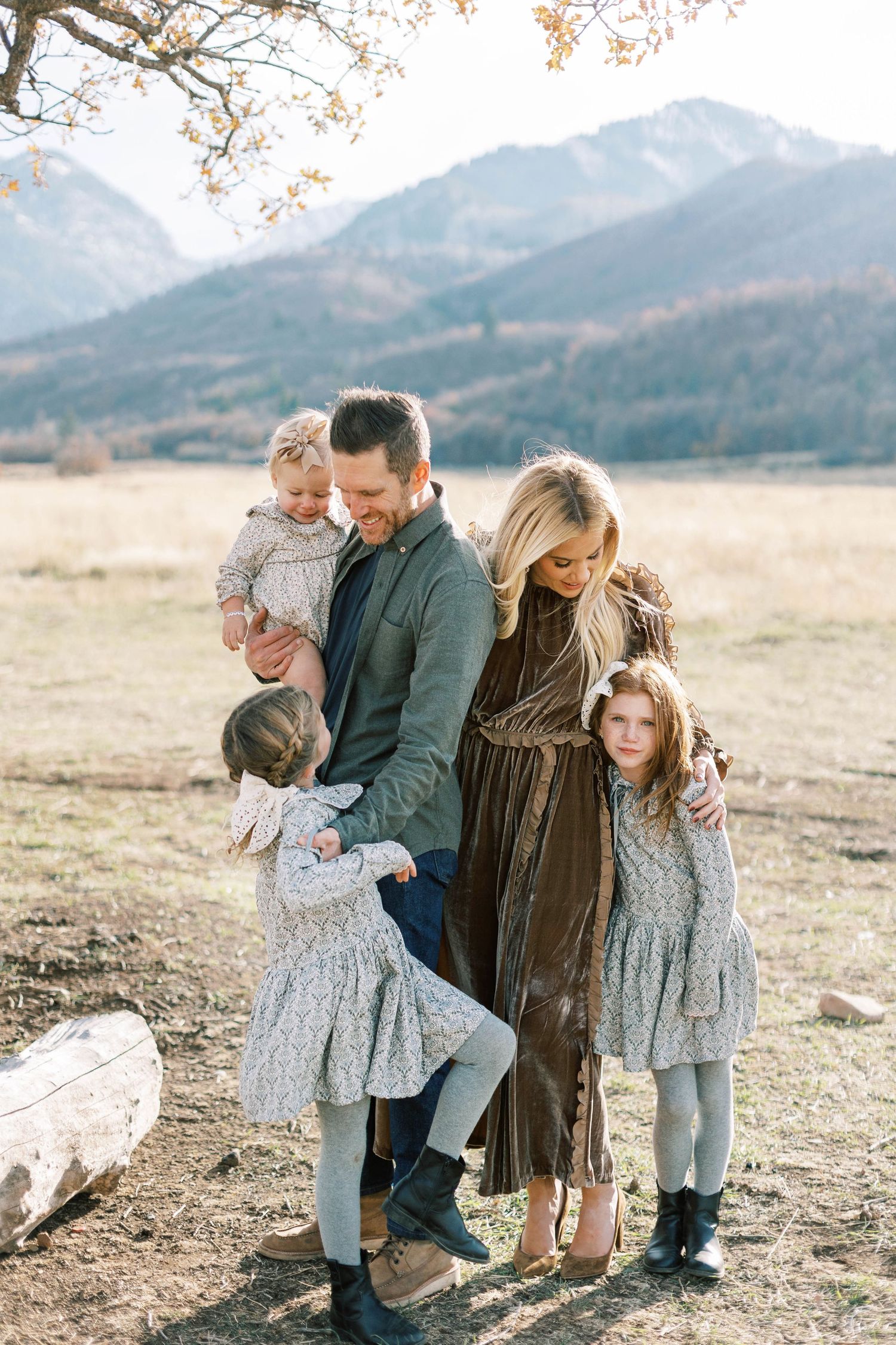Family embracing outdoors with mountain landscape and fallen log in background.