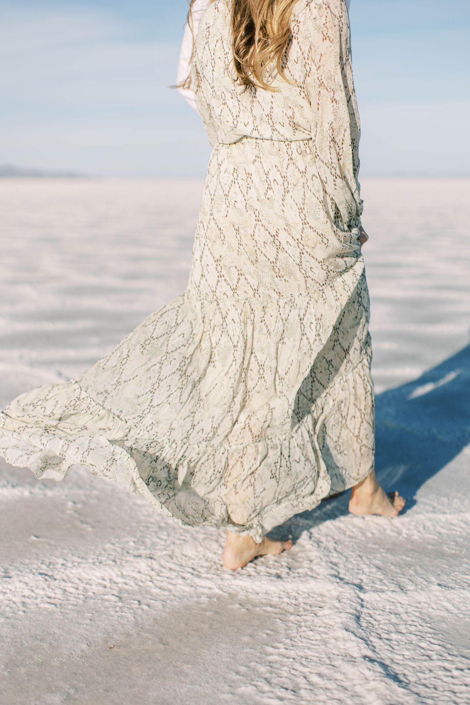 A flowing white lace dress blowing in the wind on snowy white salt flats against a bright blue sky.