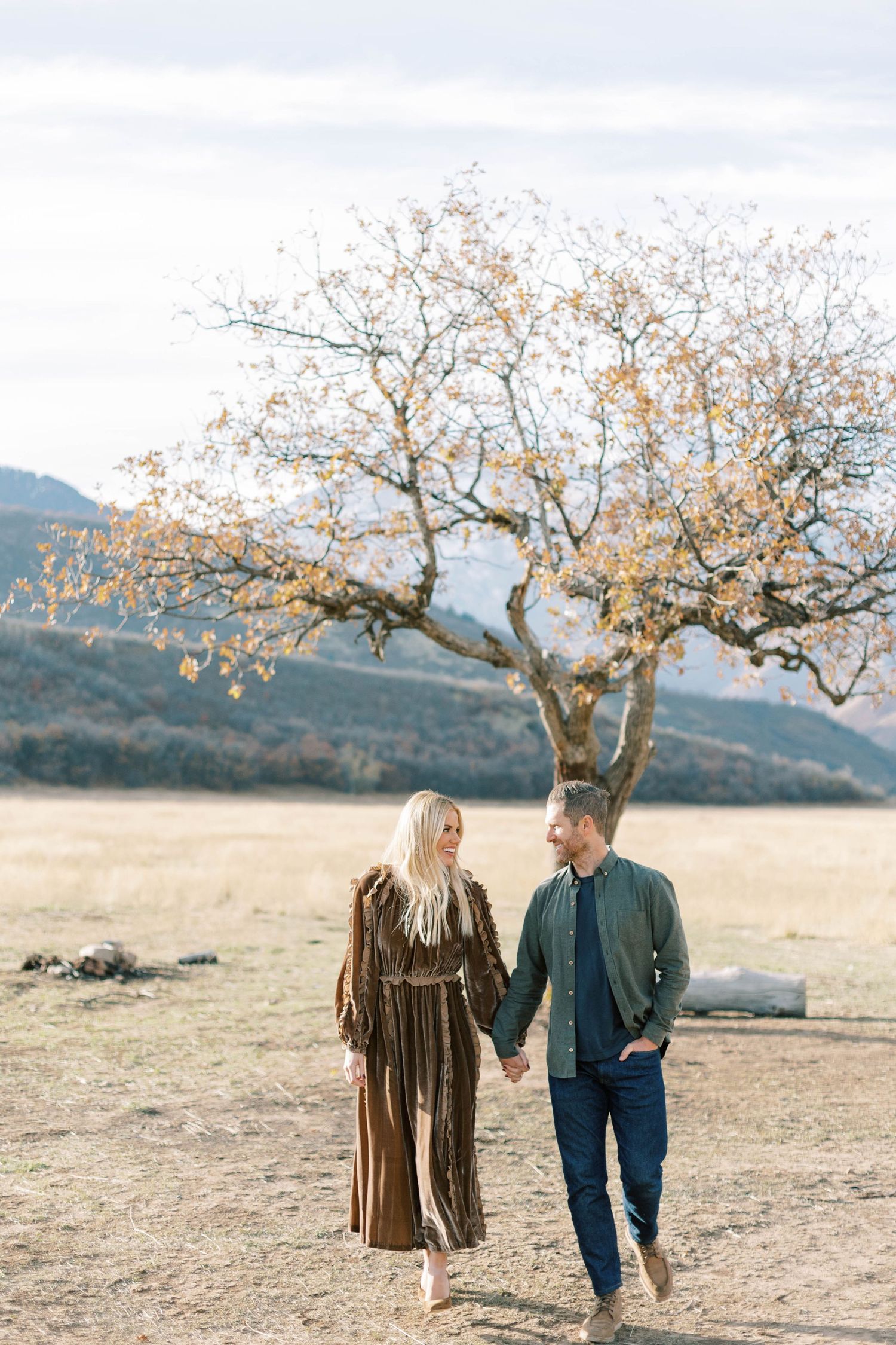 Couple takes romantic walk under blooming tree in mountain meadow landscape.