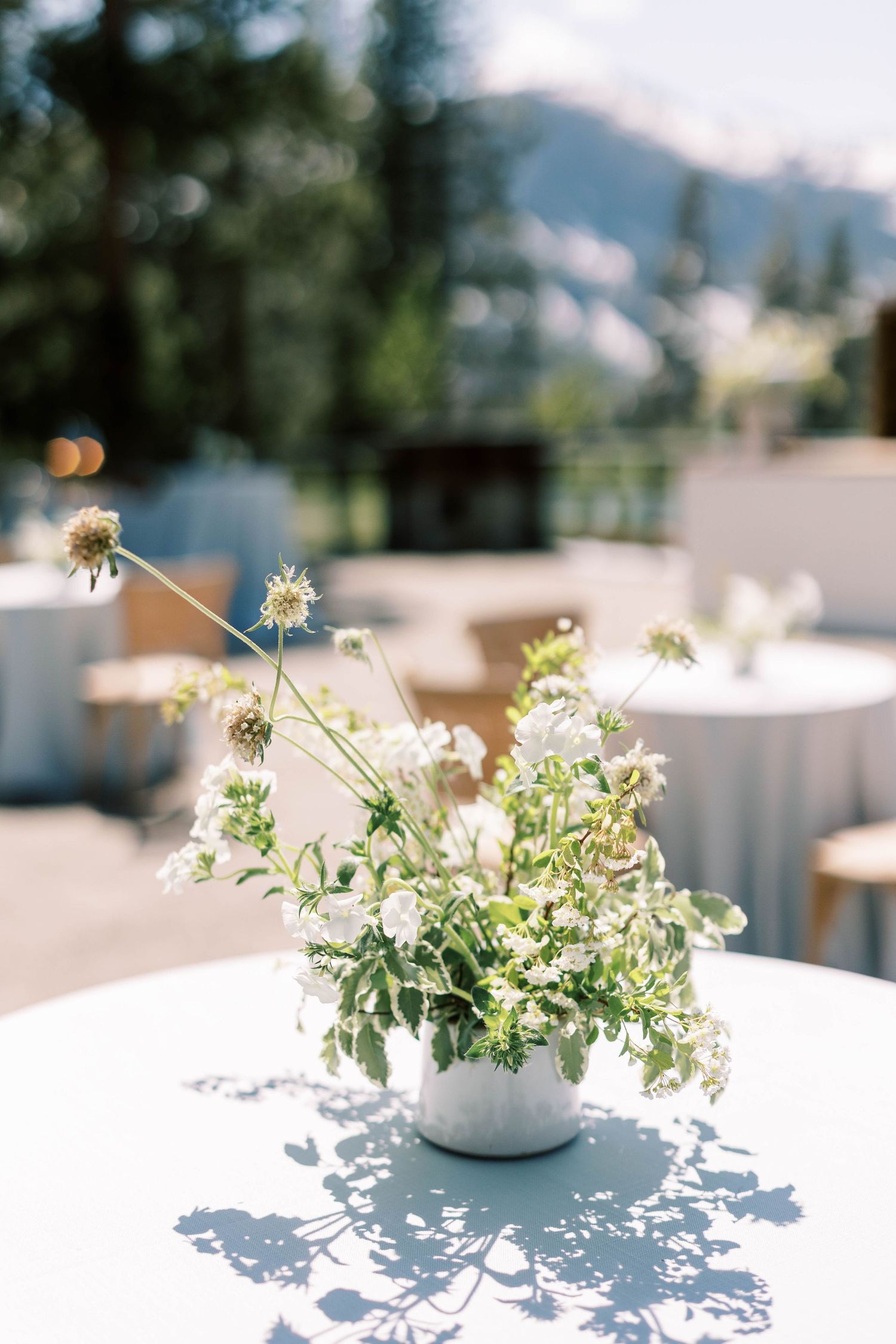 White wildflower centerpiece arrangement casting shadows on outdoor table.