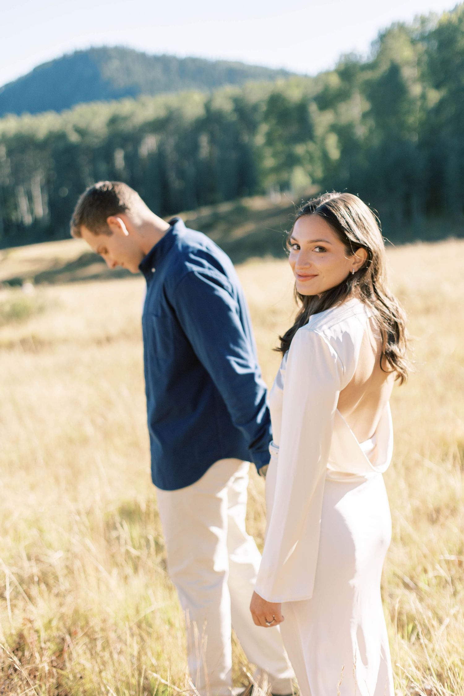 Candid moment between couple in coordinated outfits against mountain landscape.