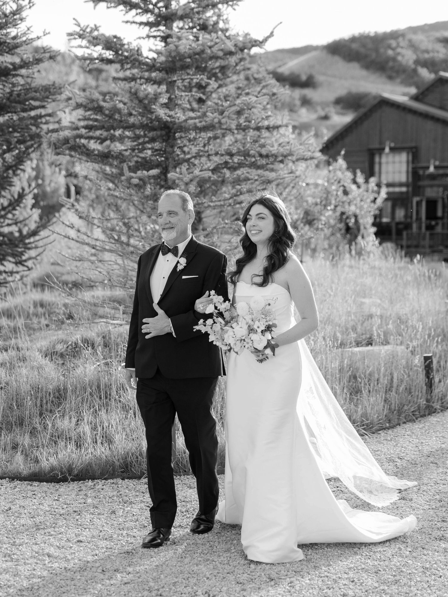 Black and white wedding portrait on rustic mountain path with natural scenery.
