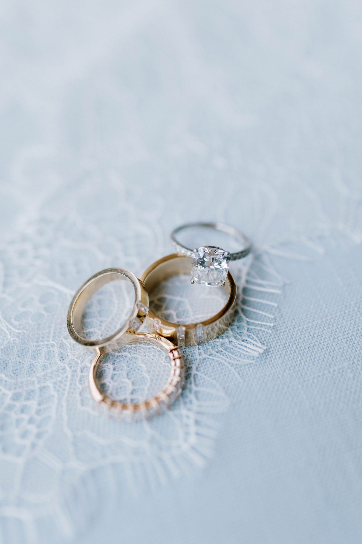 Three elegant engagement rings with diamonds and different metal bands displayed on delicate white lace fabric.