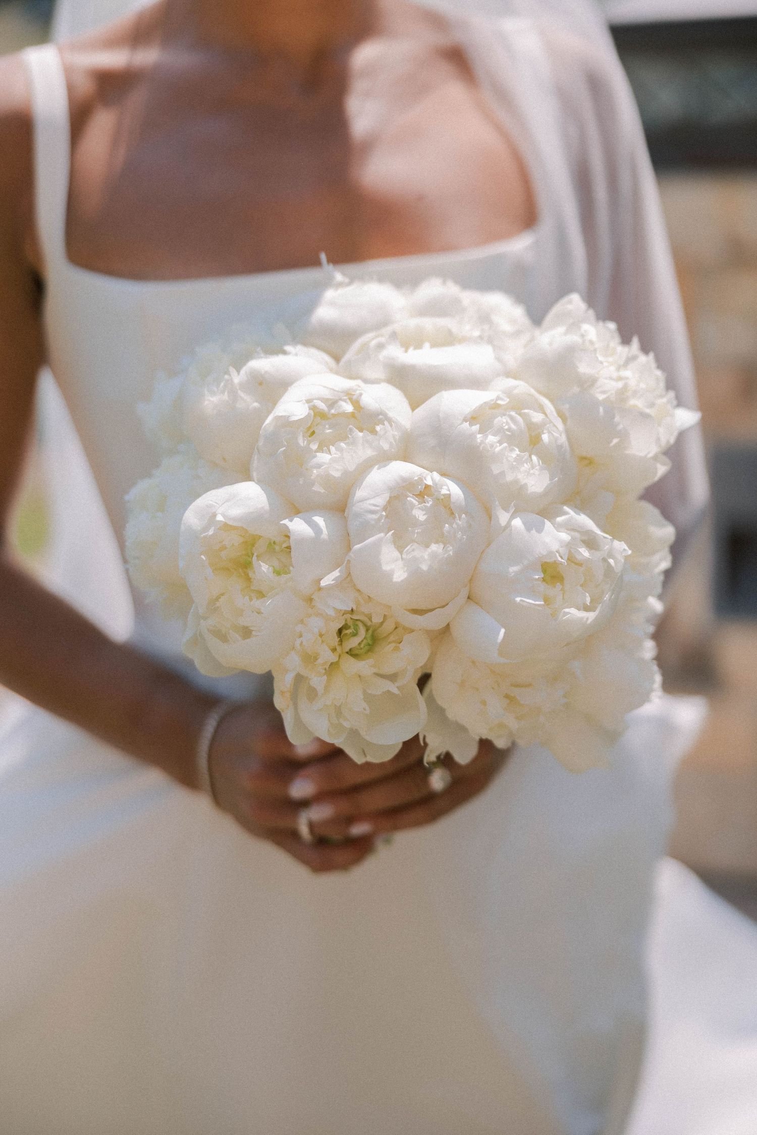 A close-up view of delicate white peonies held in hands against a white wedding dress background.
